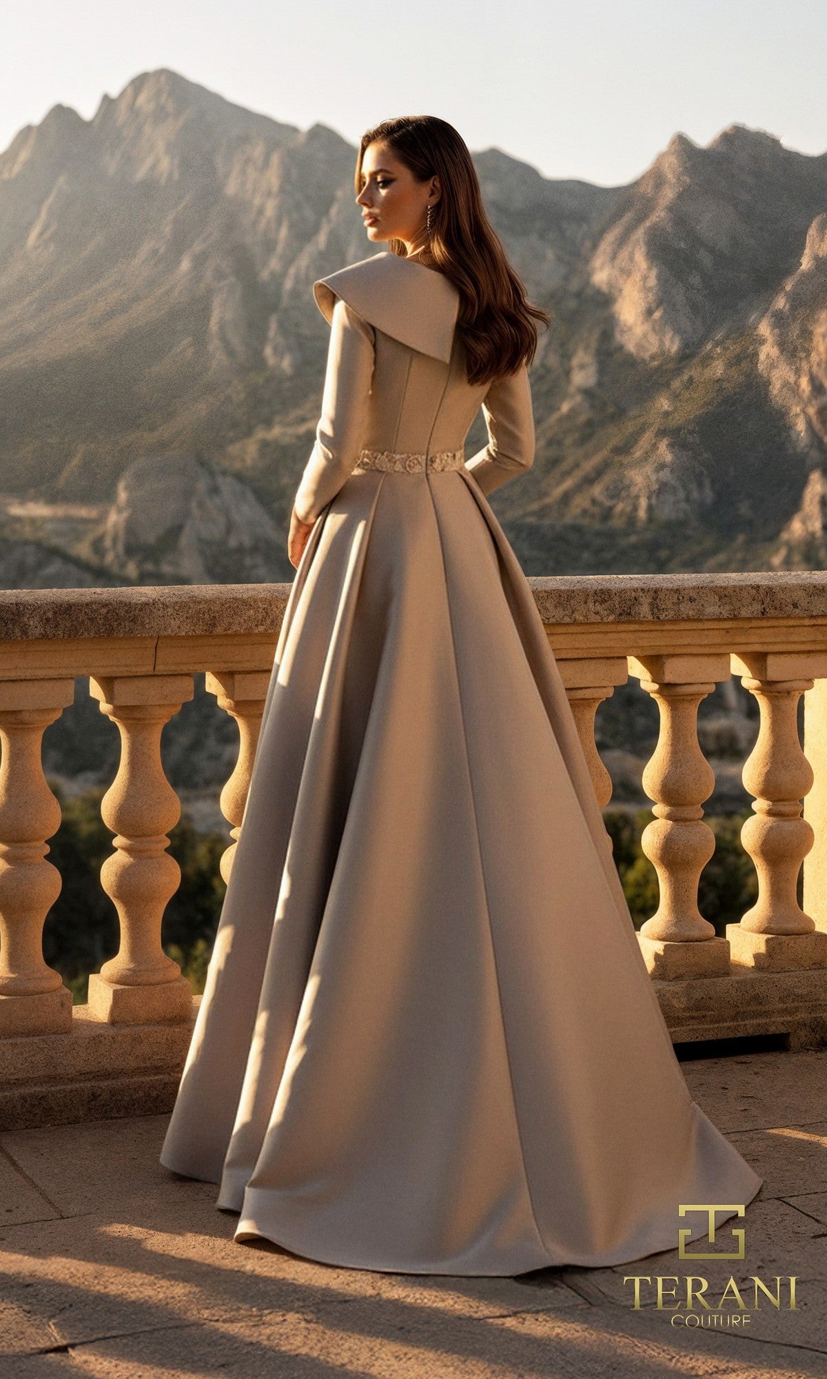 A woman in the Terani 261M6455 long formal dress made from Mikado fabric stands on a stone terrace with mountains behind her. The mother-of-the-bride gown features structured shoulders and a fitted waist.