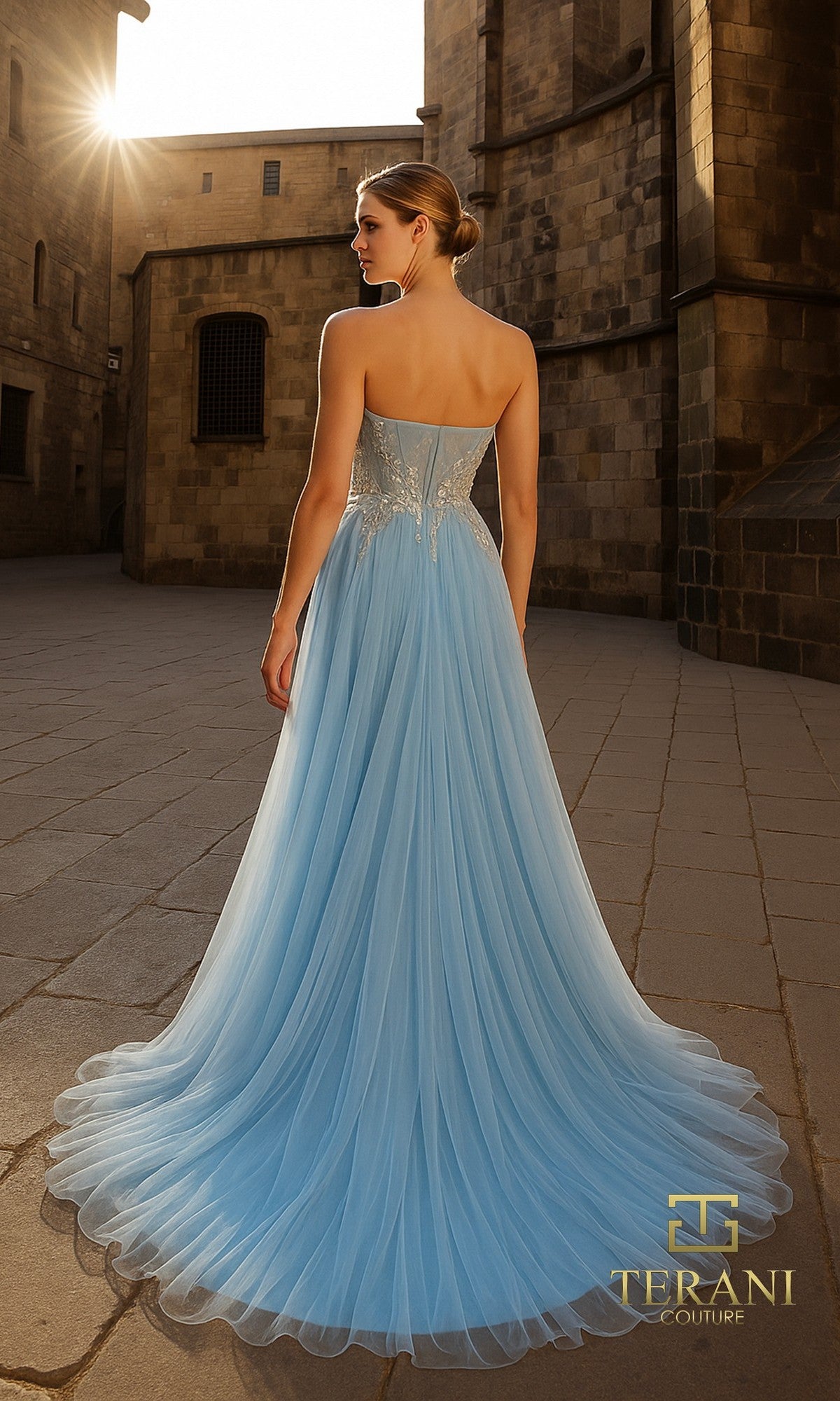 A woman stands outdoors on a stone path in sunlight, wearing the Long Formal Dress: Terani 261P6631?a light blue strapless tulle A-line gown with a fitted bodice and flowing skirt.