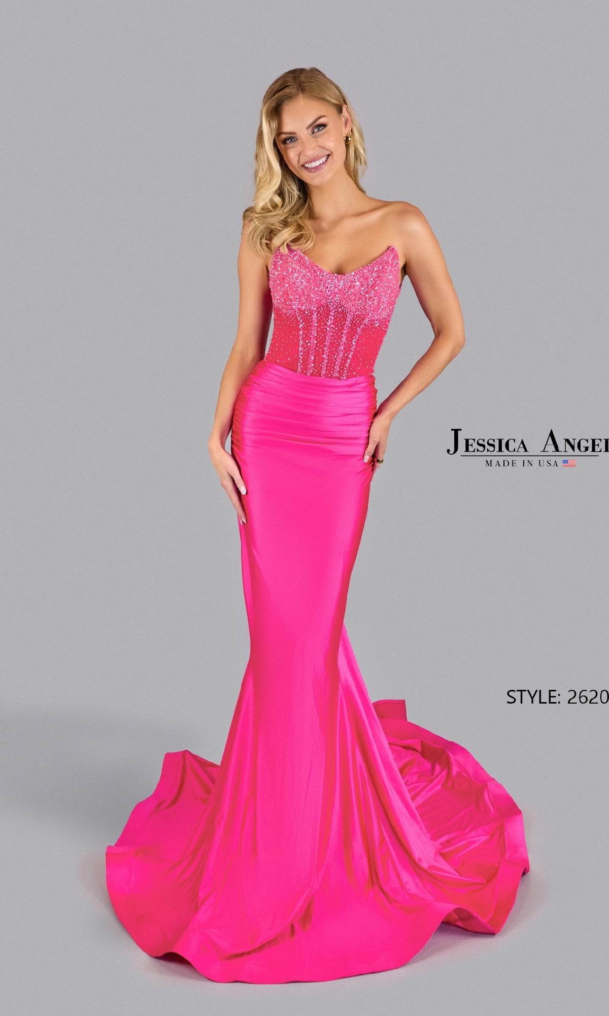 A woman poses against a plain gray background in the Jessica Angel 2620 Strapless Corset Prom Gown, featuring a bright pink beaded bodice, mermaid silhouette, sheer corset details, and a flowing train.