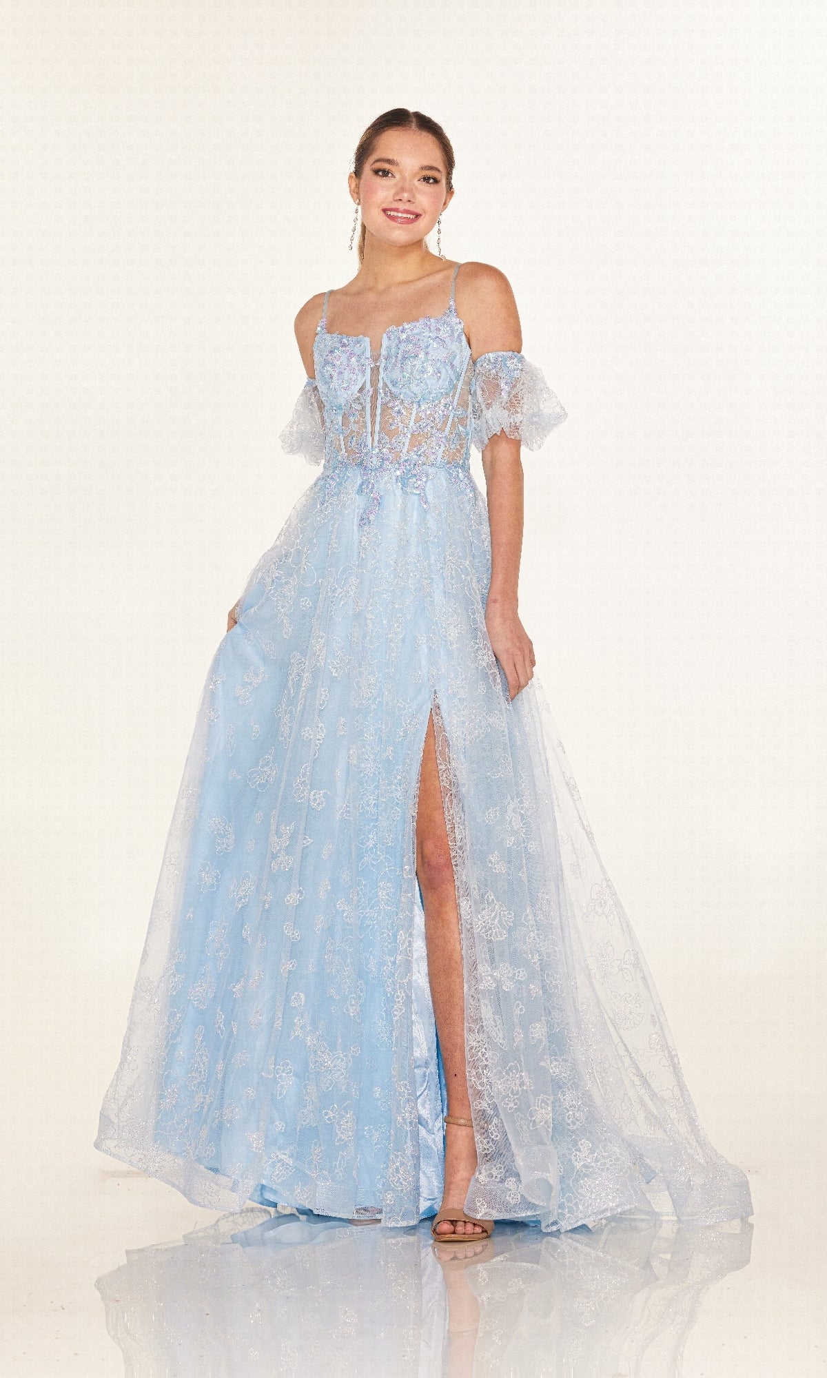 A woman wearing the Cecilia Couture 2620 long prom dress with a pastel hue, sheer corset bodice, lace details, and high slit, stands and smiles at the camera.