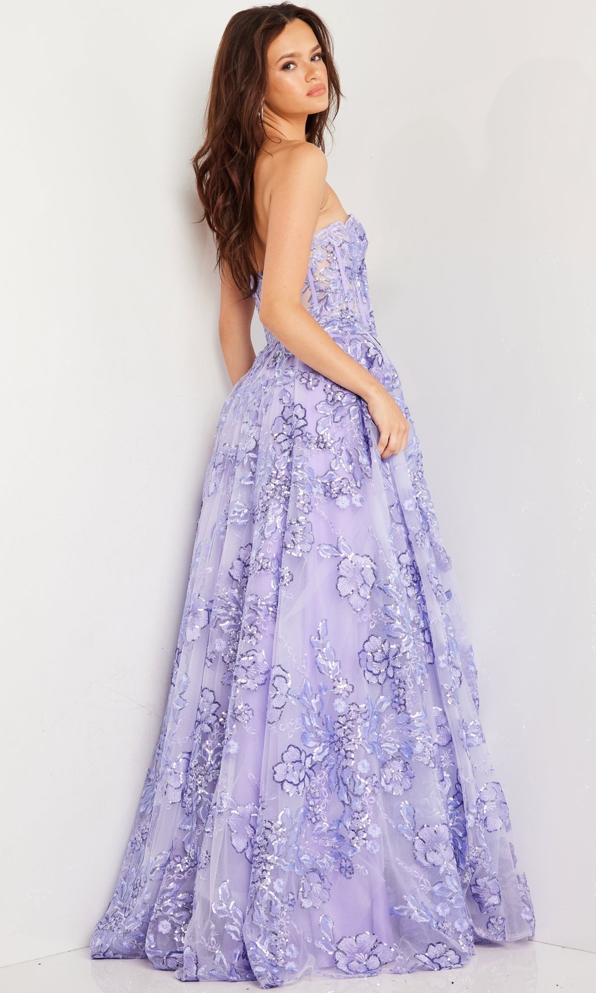 A woman models the Jovani Strapless Lilac Long Prom Ball Gown 26223, featuring floral embroidery, while standing sideways against a white background and looking over her shoulder.