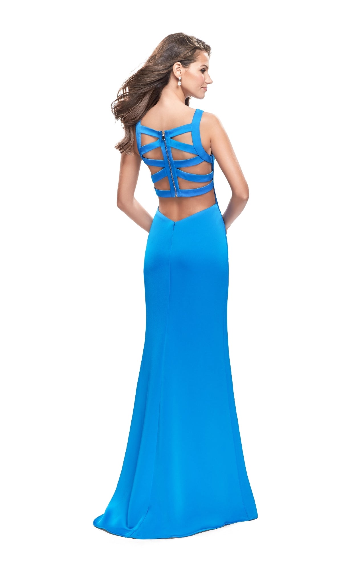 A woman stands facing away, wearing the Long Prom Dress: La Femme 26235—a fitted, floor-length bright blue gown with a strappy open back and multiple horizontal cutouts.