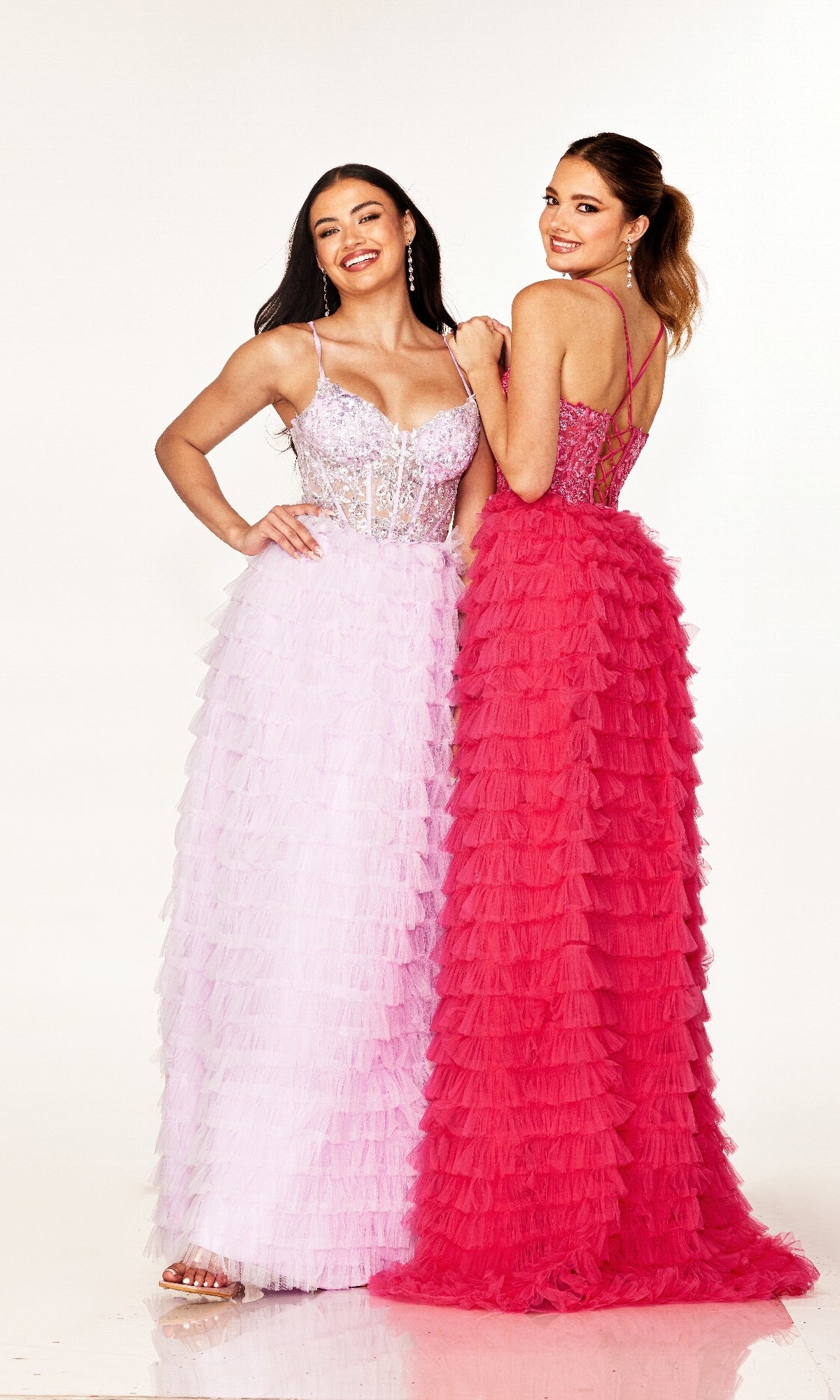 Two women stand side by side, smiling in Cecilia Couture 2624 long prom dresses—one light pink, one bright pink—with delicate ruffles and a lace-up back, both set against a plain white background.