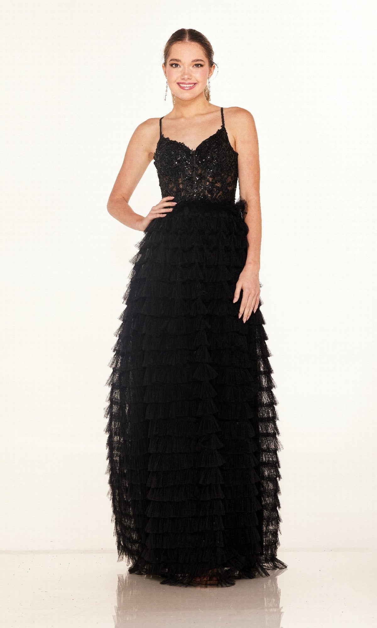 A woman stands smiling in the Cecilia Couture 2624 long black A-line prom dress, featuring thin straps, lace detailing, and a sheer corset bodice, against a plain white background.