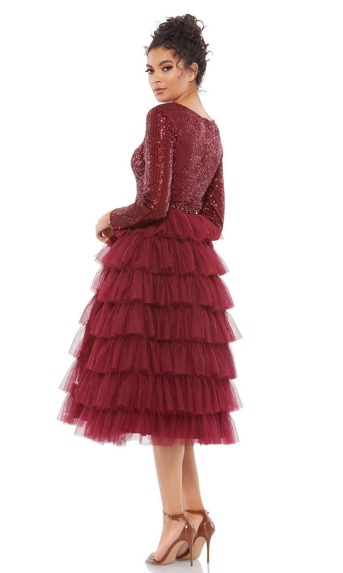 A woman stands in profile wearing the Mac Duggal 26299 Knee-Length Wedding Guest Dress, featuring a burgundy sequined top and a tiered tulle A-line skirt, paired with nude high-heeled sandals.