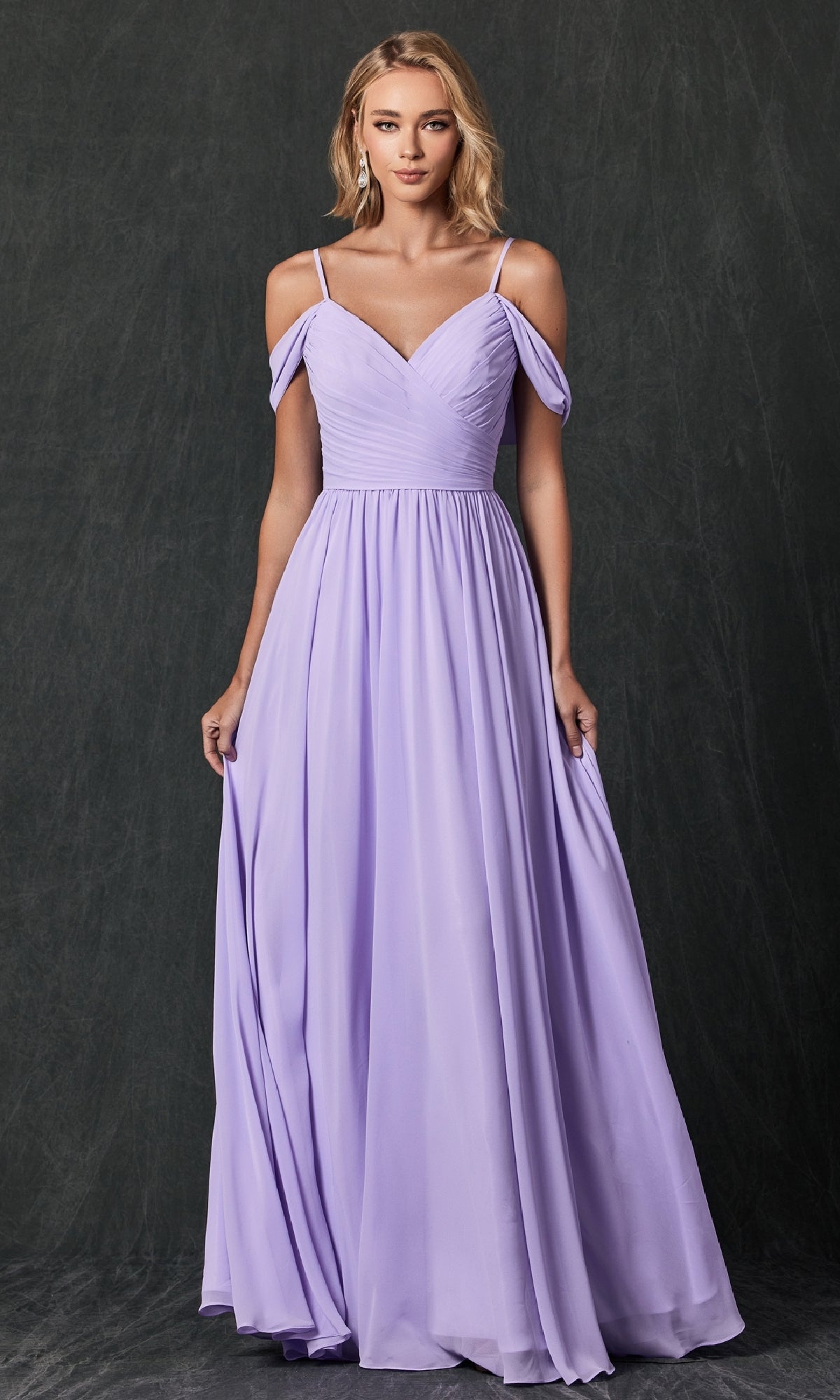 A woman wears the Juliet 262 long prom dress, a floor-length, light purple A-line gown with off-the-shoulder straps, standing against a dark, textured background.