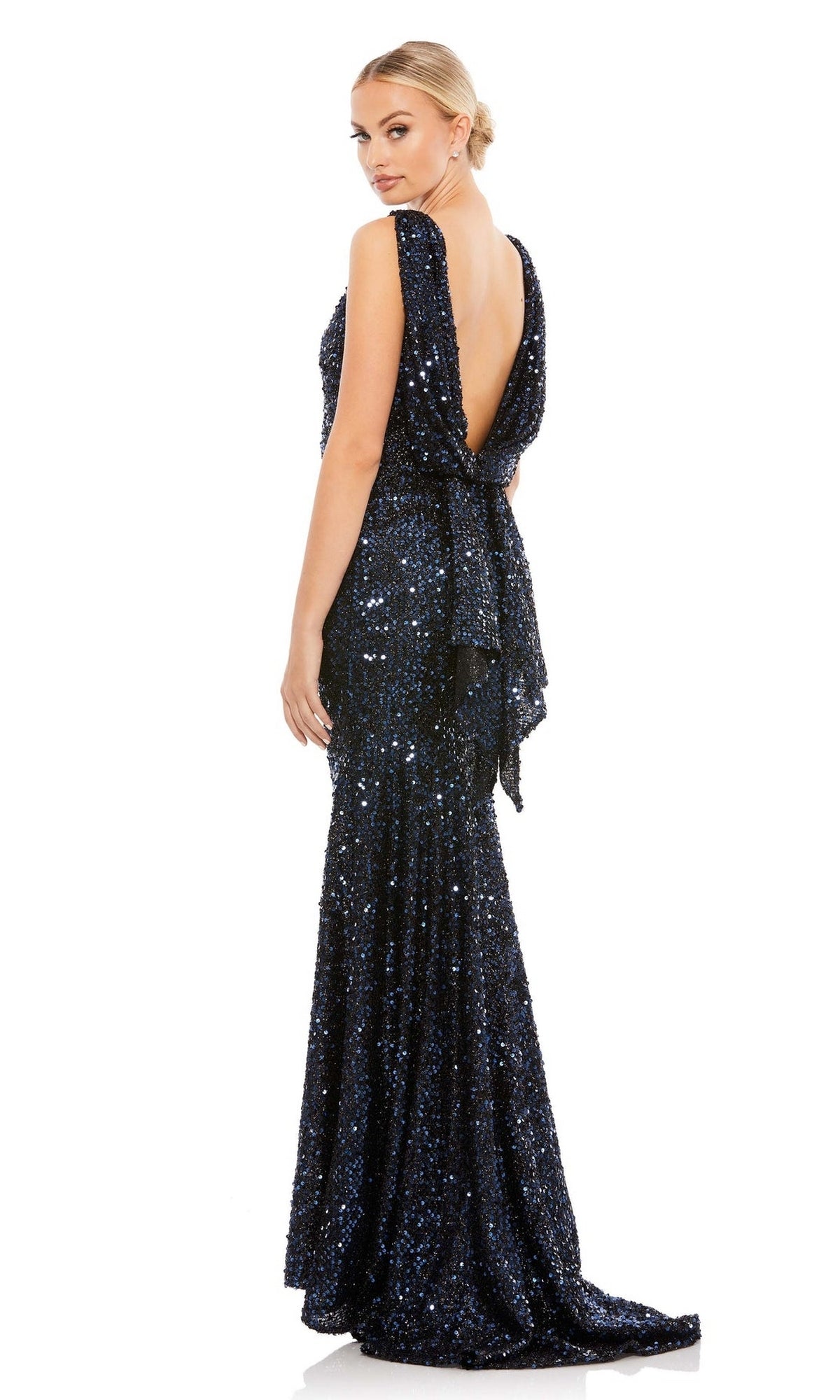 Woman wearing a floor-length, navy blue Mac Duggal 26331 cowl-back long sequin prom dress, looking over her shoulder against a white background.