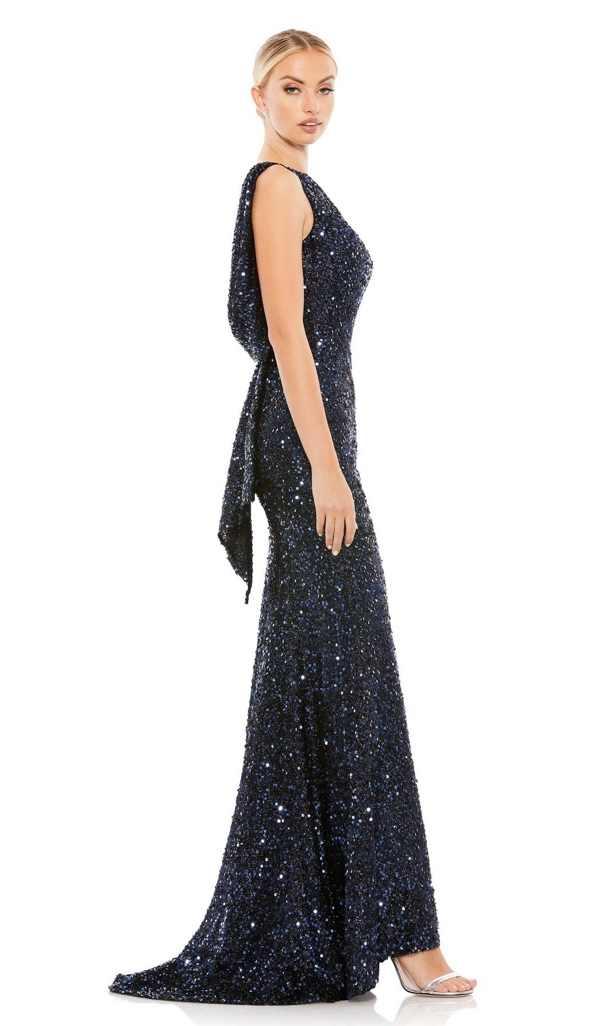 Woman in profile wears the Mac Duggal 26331 Cowl-Back Long Sequin Prom Dress—a sleeveless, floor-length dark blue gown with side sash detail—posed against a white background.