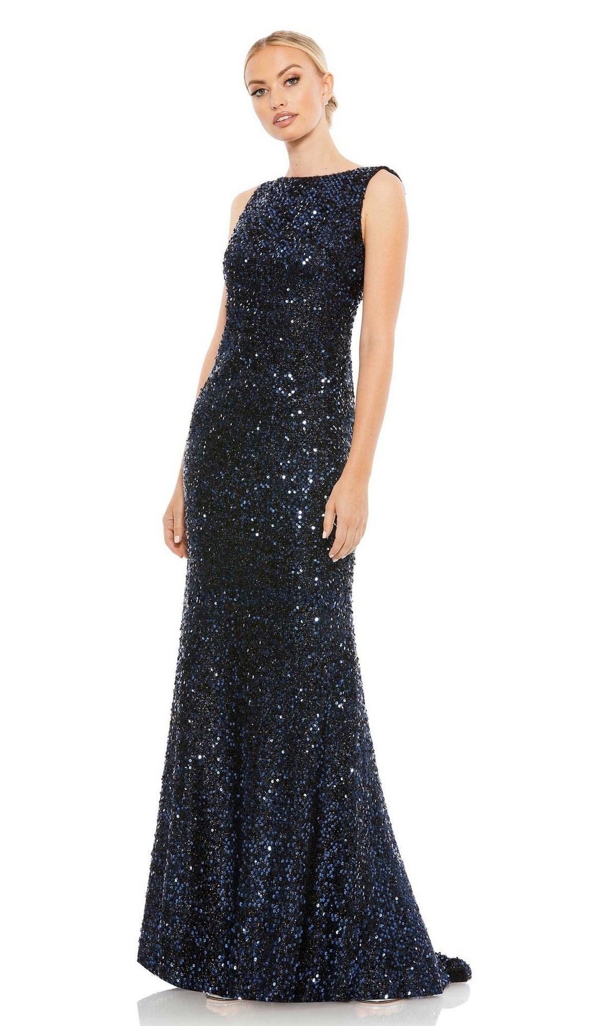A woman stands against a white background wearing the Mac Duggal 26331 Cowl-Back Long Sequin Prom Dress, a stunning navy blue, floor-length, sleeveless gown.