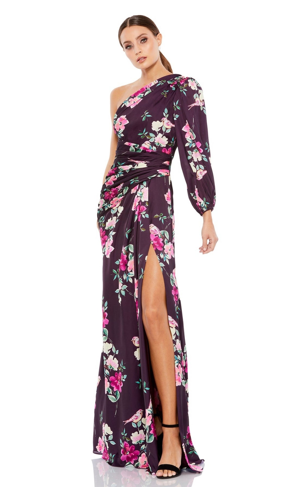 A woman poses against a white background wearing the Mac Duggal 2634—a plum floral long formal dress with one shoulder, long sleeve, high side slit—paired with black high-heeled sandals.