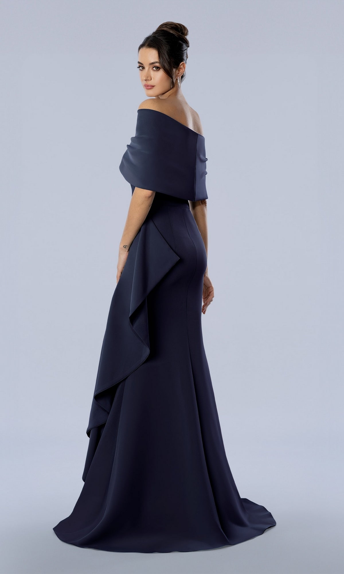 A woman wearing the Long Formal Dress: Stella Couture 26372, a dark navy off-the-shoulder floor-length gown with a draped ruffle detail at the hip.