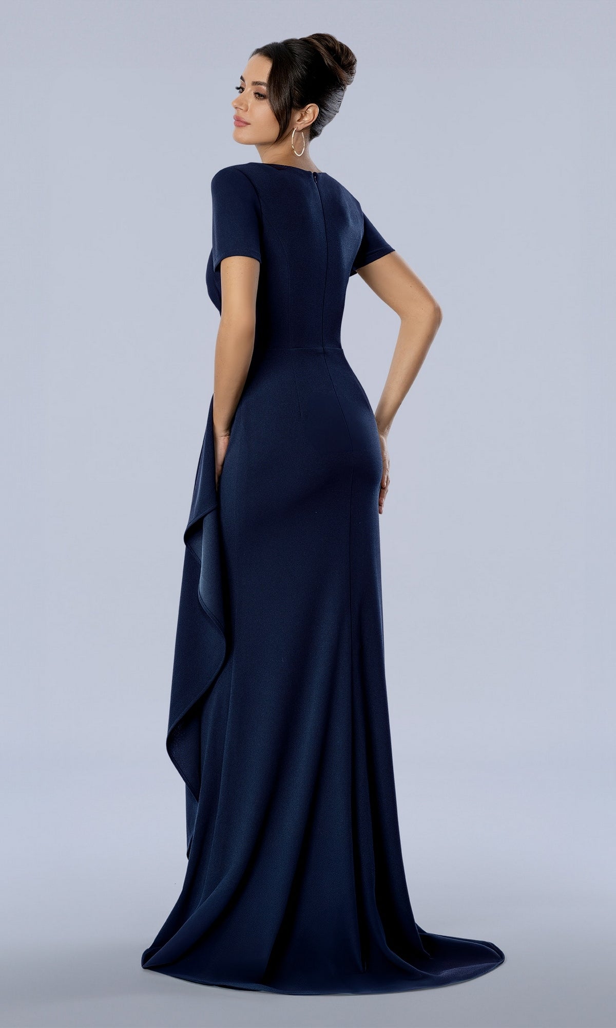 A woman wears the navy Stella Couture 26376 long formal dress, a floor-length navy blue gown with short sleeves and a draped side detail.