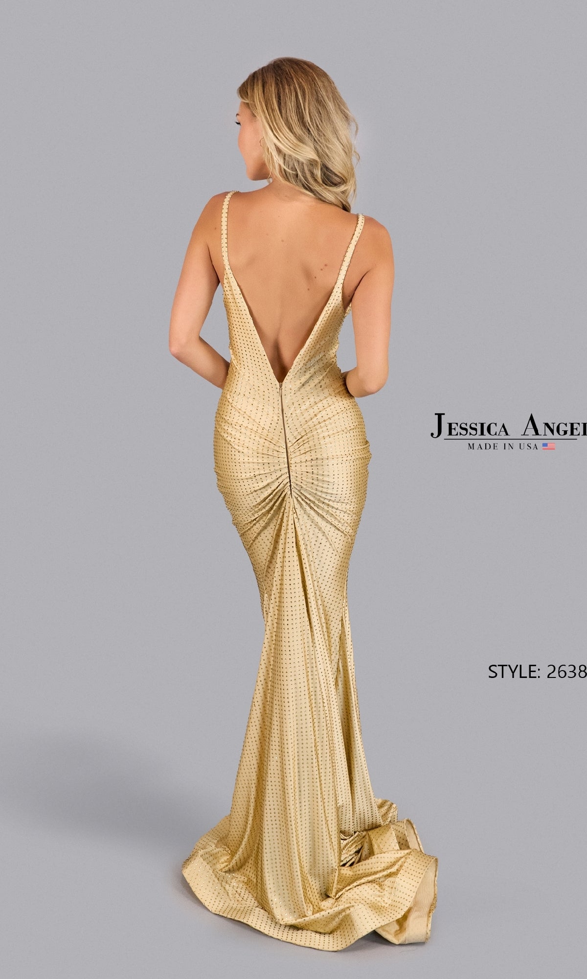 Woman in the Empire-Waist Beaded Prom Dress: Jessica Angel 2638, a gold floor-length gown with a deep V-back and ruched detailing, standing against a plain gray background.