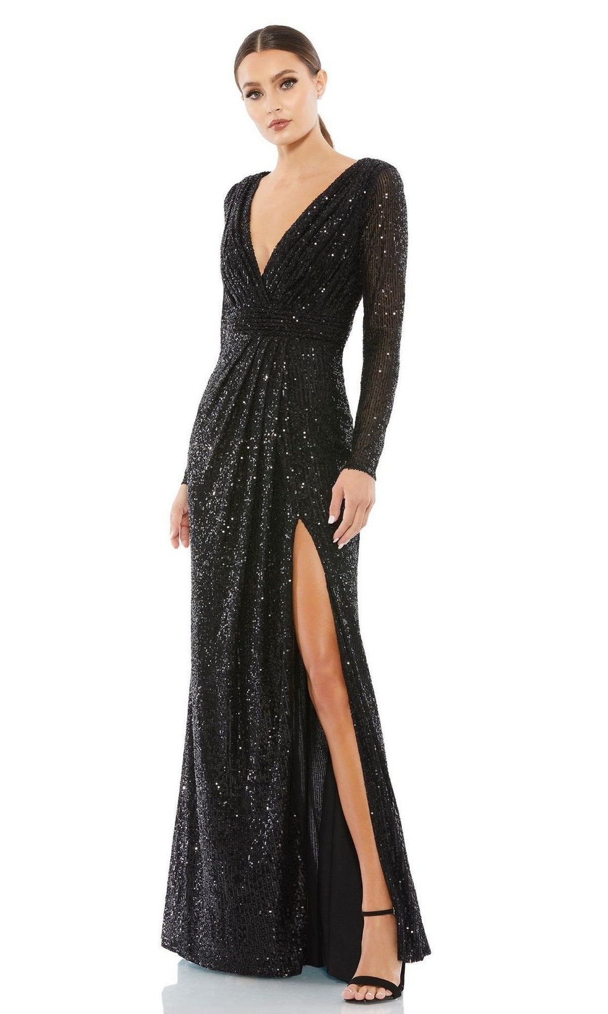 A woman wearing the Mac Duggal 26490 long-sleeve formal dress featuring black sequins, a deep V-neckline, and a high slit, styled with black heels.