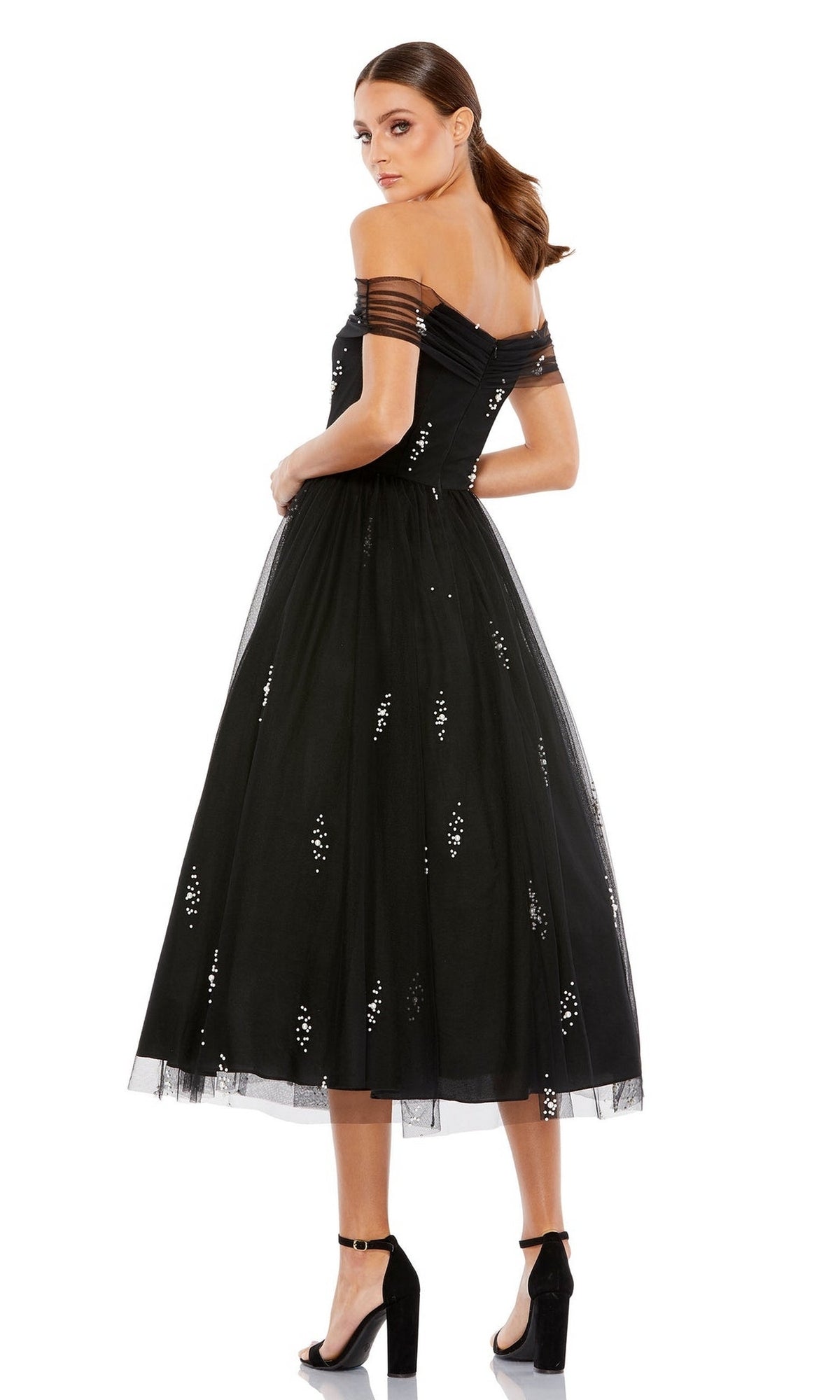 Woman wearing the Mac Duggal 26498 Black Midi Wedding-Guest Dress with an off-the-shoulder neckline, tulle skirt, and sequin accents, styled with black high-heeled sandals.