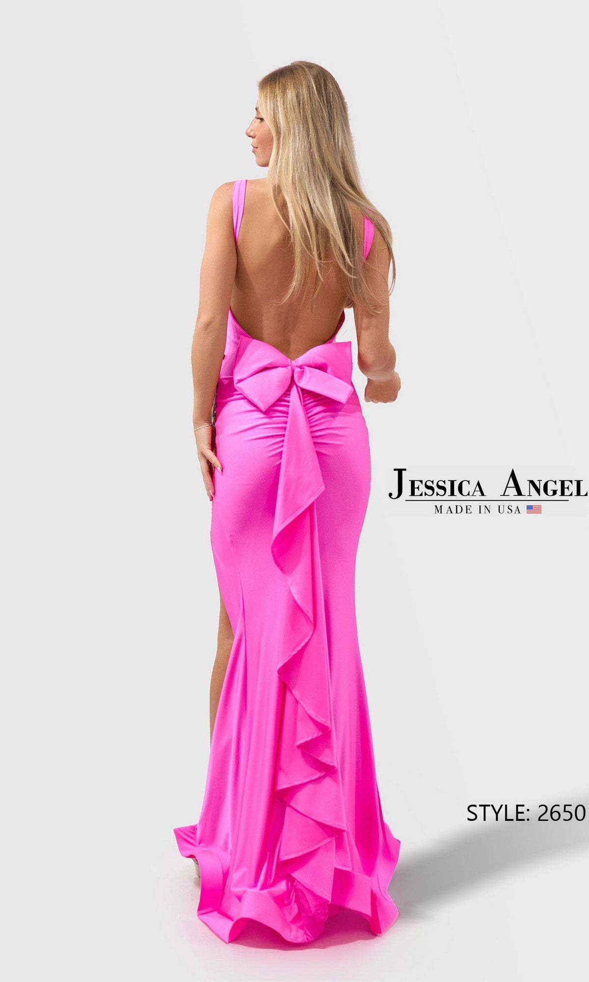 A woman models the Jessica Angel 2650 long prom dress in bright pink stretch jersey, featuring a sleeveless design with a large bow and ruffle detailing down the back, posing with her back to the camera.