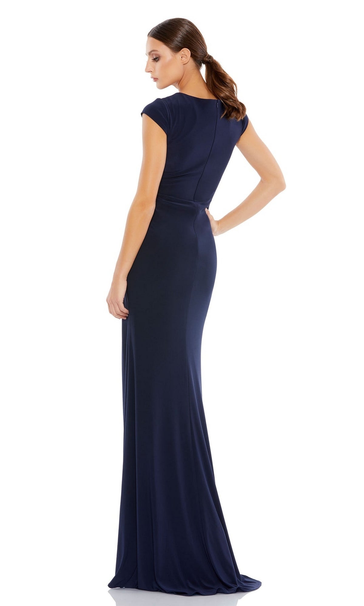 A woman models the Long Formal Dress 26504 by Mac Duggal—a fitted, floor-length navy gown with cap sleeves and a v-neckline—standing in a side-back pose against a plain white background.
