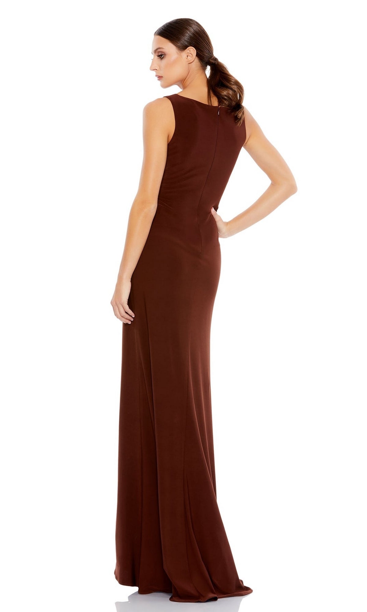 A woman faces away, wearing the Mac Duggal 26513 Faux-Wrap Long Formal Dress—a sleeveless, floor-length fitted brown gown. Her hair is styled in a low ponytail.