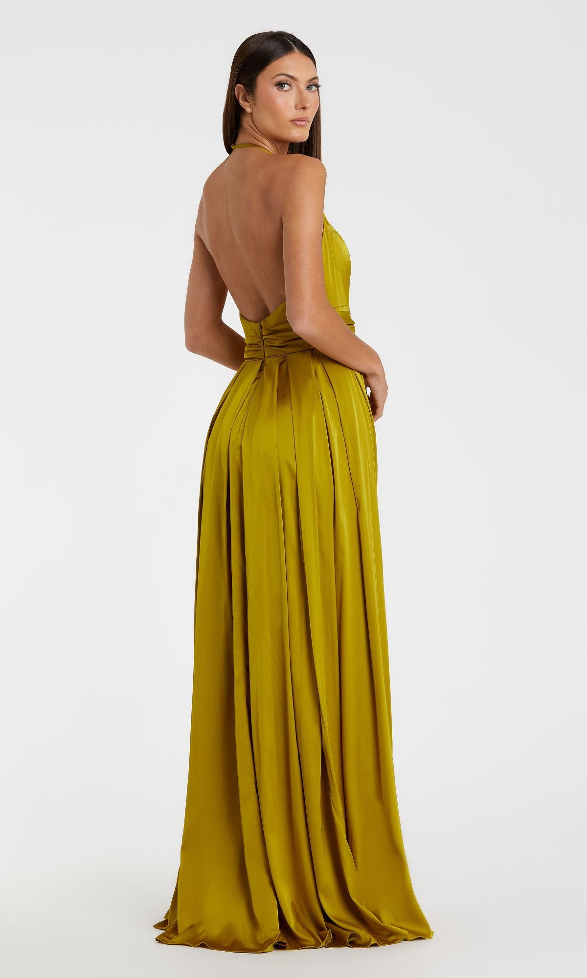 A woman models the Mac Duggal 26531 Bowed Long Halter Formal Dress in yellow-gold satin, backless style, standing with her back slightly turned toward the camera against a plain white background.