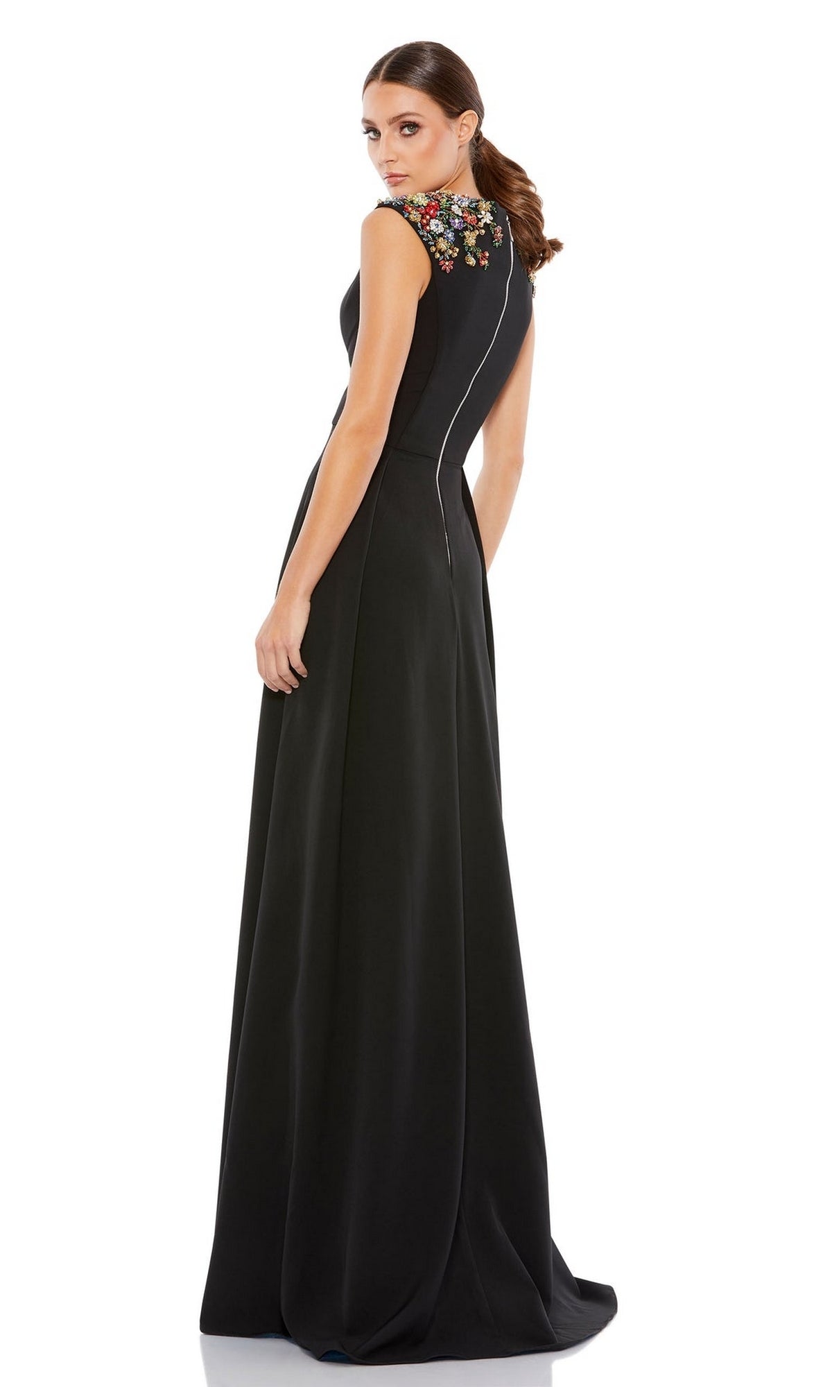 Woman in the Mac Duggal 26540 Cap-Sleeve Long Formal Dress, a black gown with colorful floral embroidery and embellished shoulders, standing and looking over her shoulder.