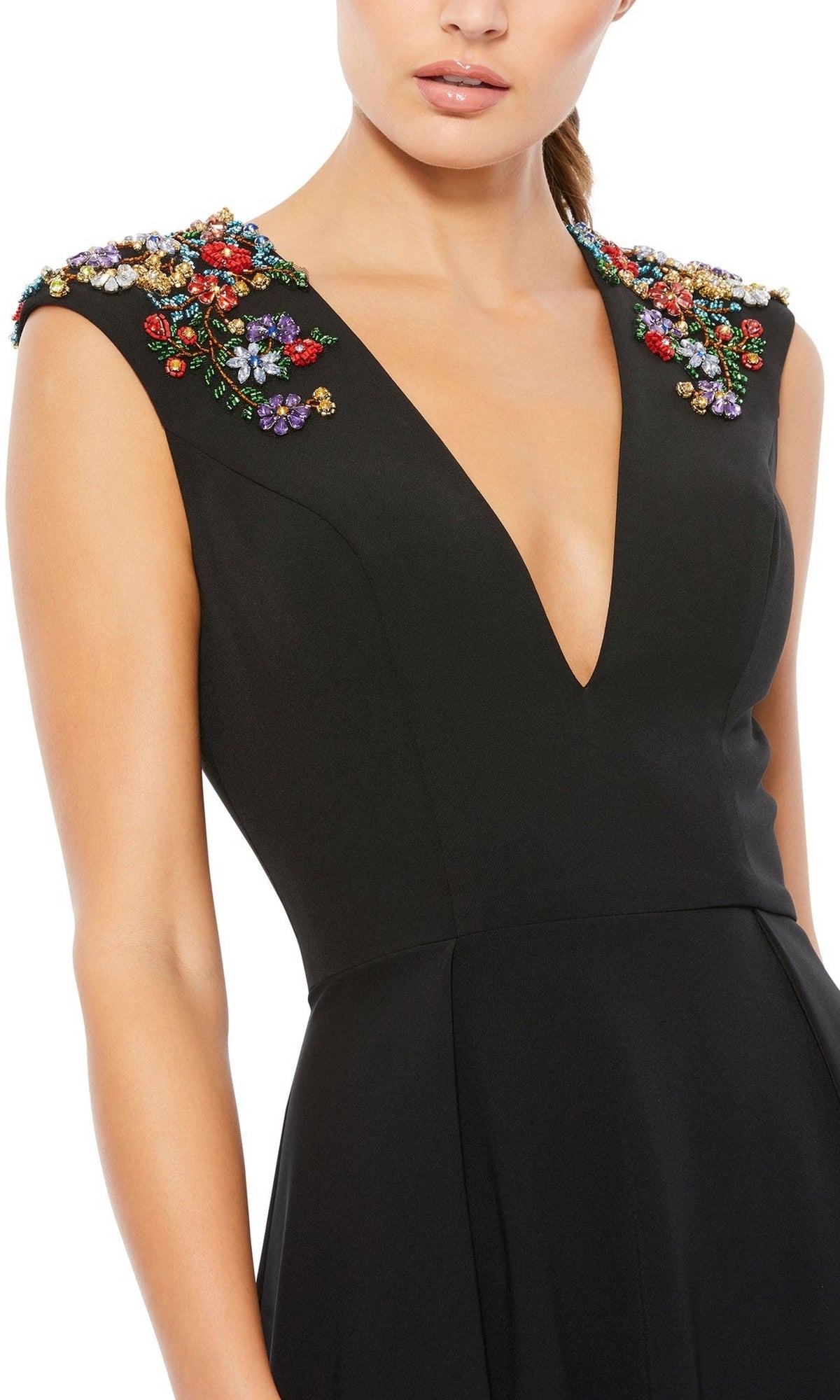 A woman wears the Cap-Sleeve Long Formal Dress, Mac Duggal 26540, featuring a deep V-neck, black sleeveless design, and colorful floral embellishments on the shoulders.