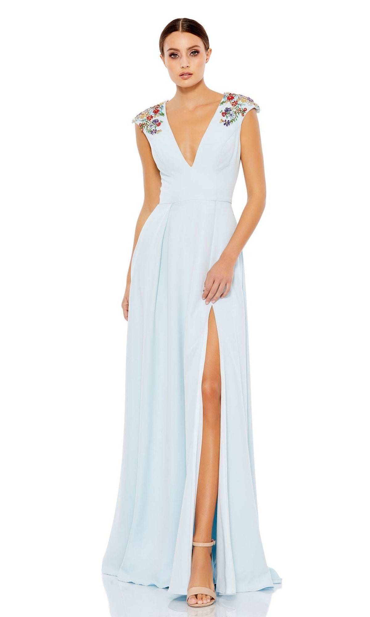 A woman stands against a white background wearing the Cap-Sleeve Long Formal Dress: Mac Duggal 26540, a light blue evening gown featuring floral embroidery, a deep V-neck, cap sleeves, and a thigh-high slit.
