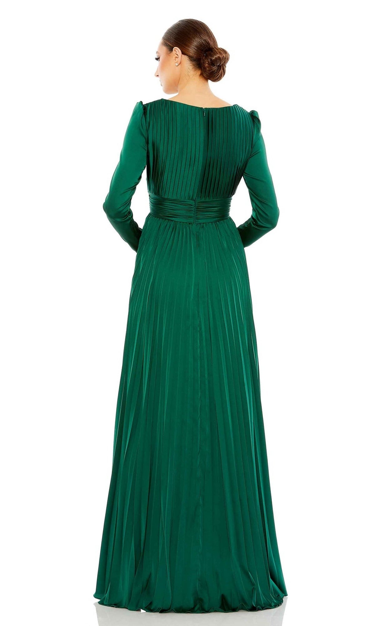 A woman stands facing away, wearing the Long Formal Dress 26542 by Mac Duggal—a long-sleeved, floor-length emerald green pleated dress with a fitted waist and v-neckline. Her hair is styled in a low bun.