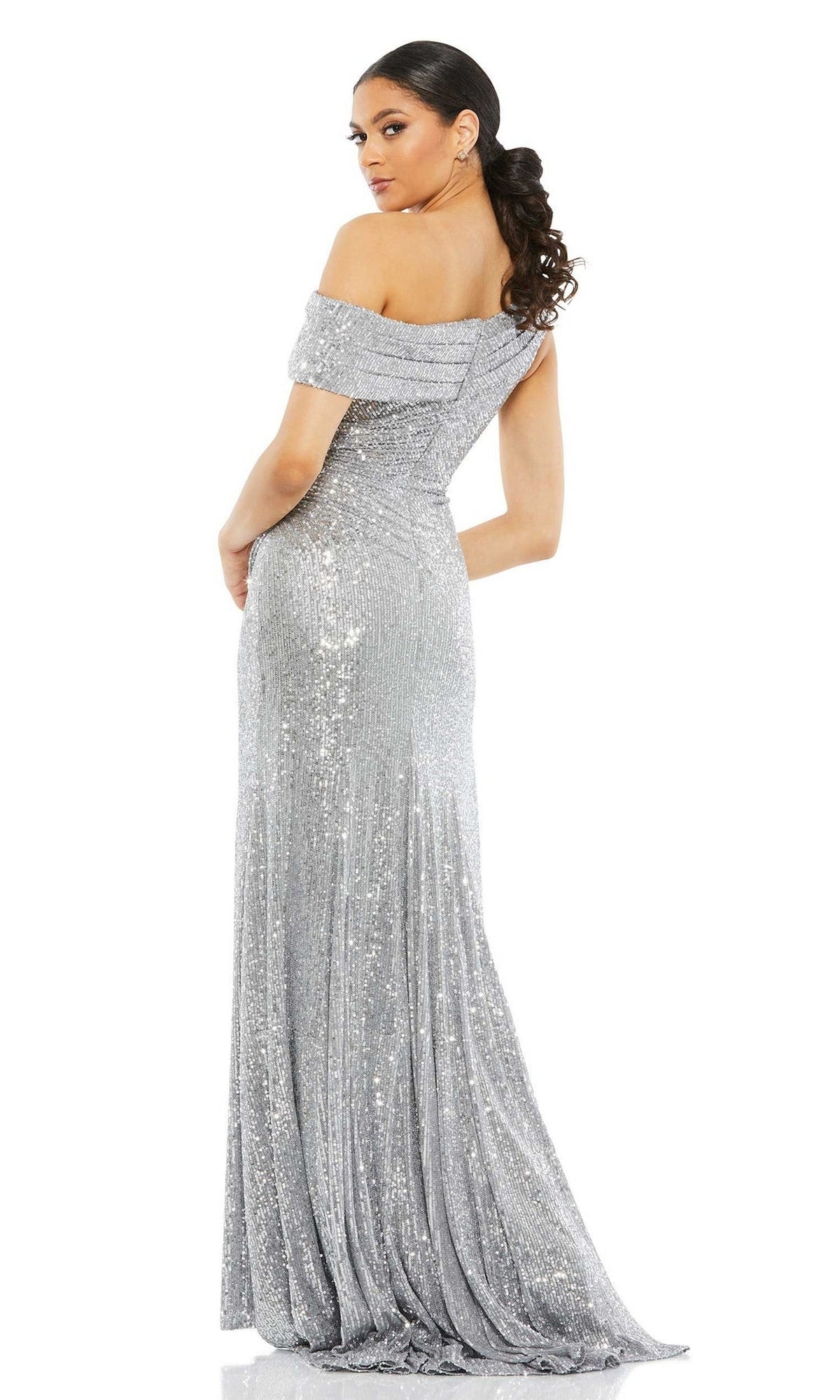A woman models the Mac Duggal 26550 Drop-Shoulder Sequin Formal Gown, a shimmering silver dress with an off-the-shoulder fitted bodice and floor-length skirt, standing partially turned to showcase the elegant design.