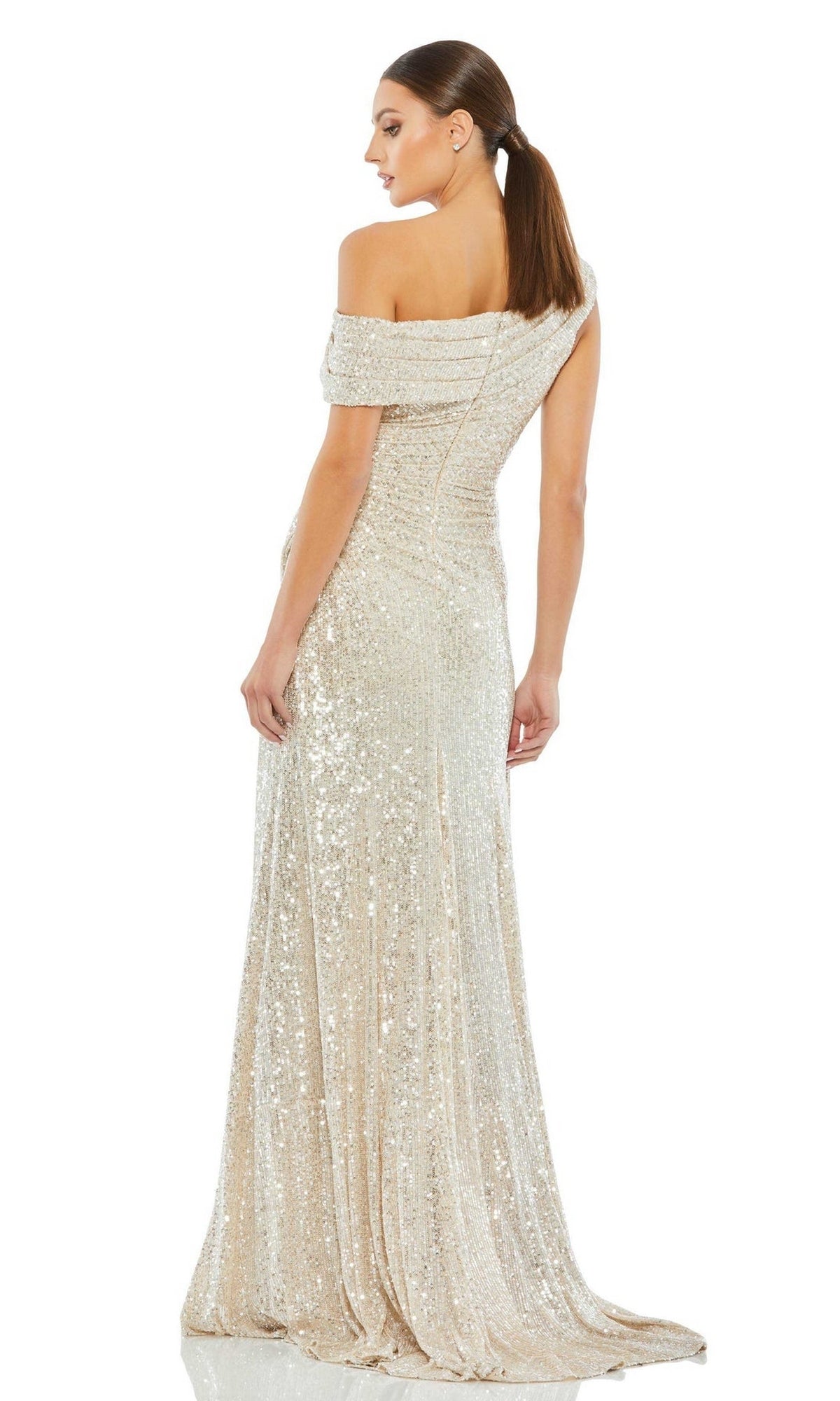 A woman stands with her back turned, looking over her shoulder in the Mac Duggal 26550 Drop-Shoulder Sequin Formal Gown, a floor-length light gold dress.