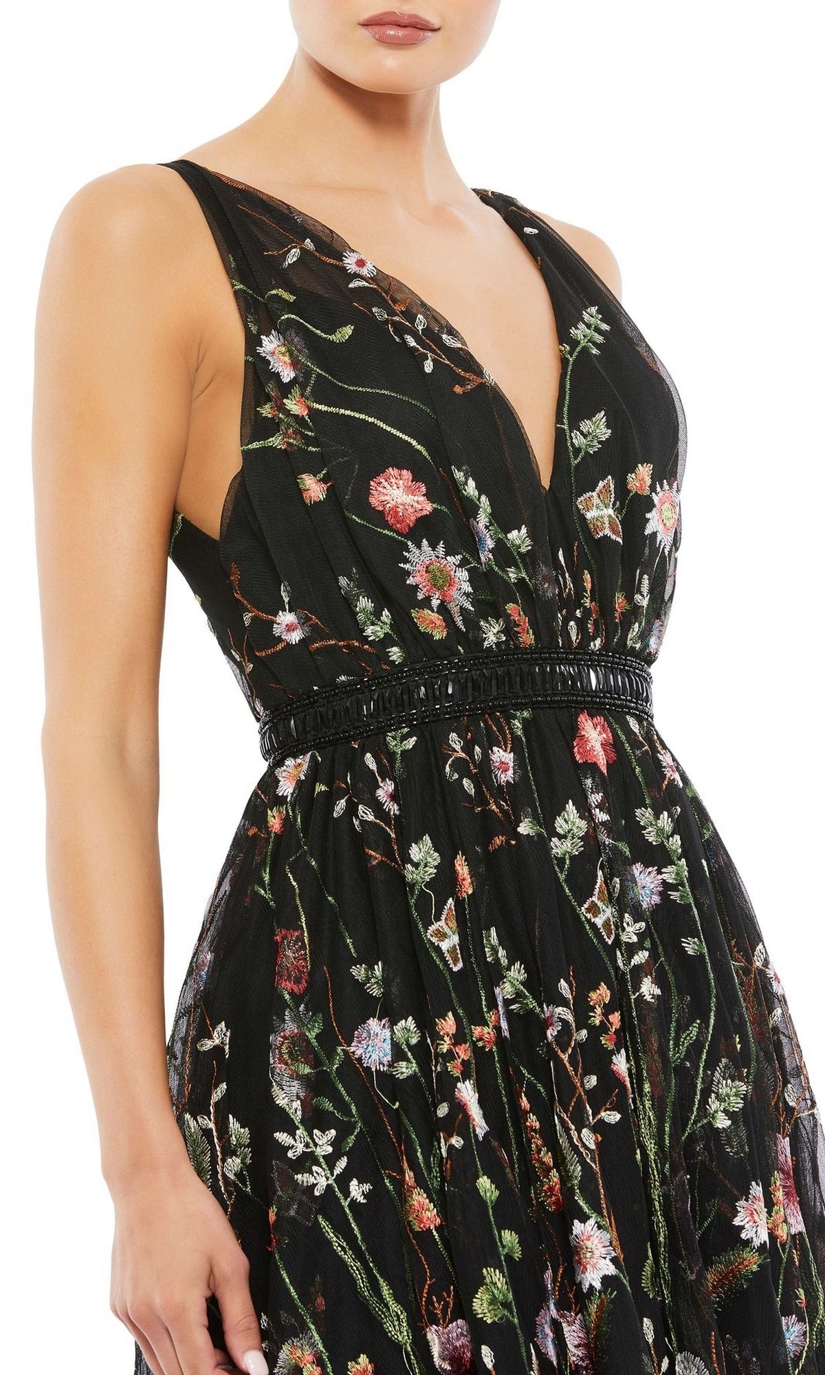 A woman wears the Mac Duggal 26557 Black Floral Wedding Guest Dress, a sleeveless black dress with a deep V-neck and multicolored floral embroidery—perfect for chic parties.