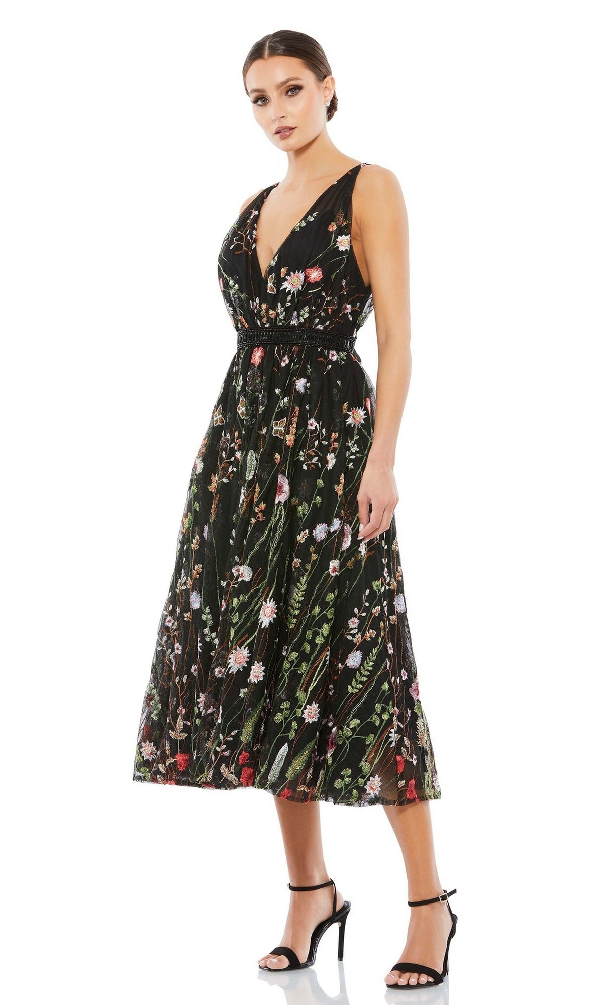 Woman in the Mac Duggal 26557 Black Floral Wedding Guest Dress with a sleeveless, deep V-neck and black high-heeled sandals, standing against a white background.
