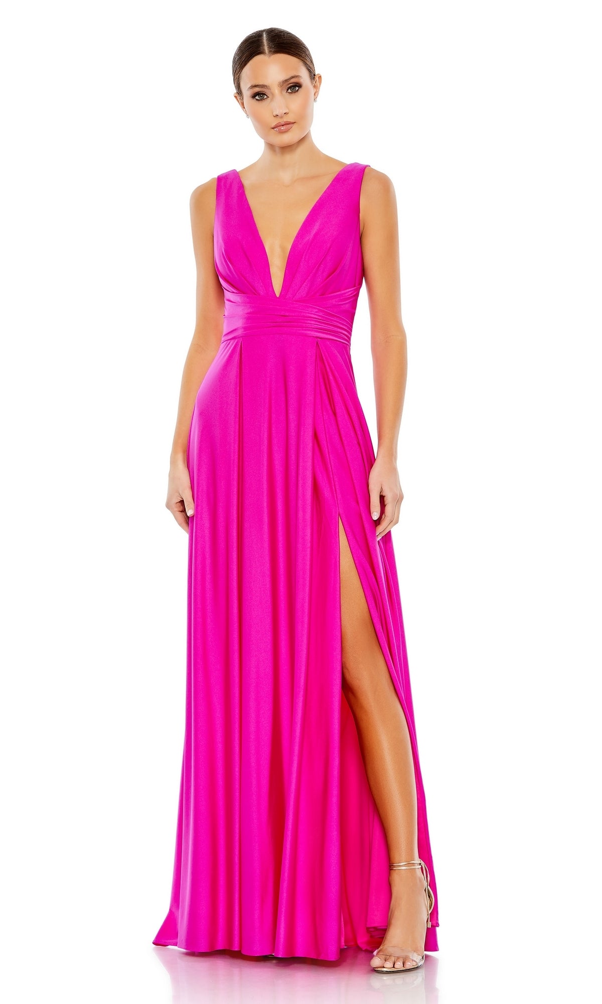 A woman wears the Mac Duggal 26578 V-Neck Long A-Line Prom Dress in bright pink, featuring a sleeveless design, deep neckline, and high slit, styled with strappy heels.