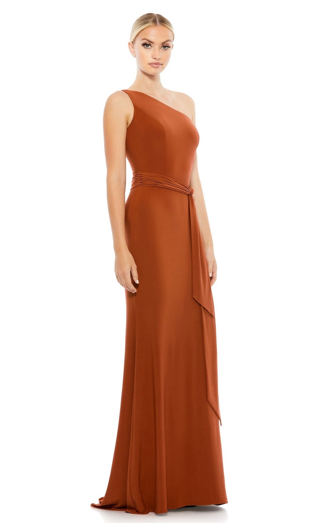A woman models the Mac Duggal 26581 Belted Long Jersey Formal Dress in rust, featuring a one-shoulder design and fitted waist, against a plain white background.