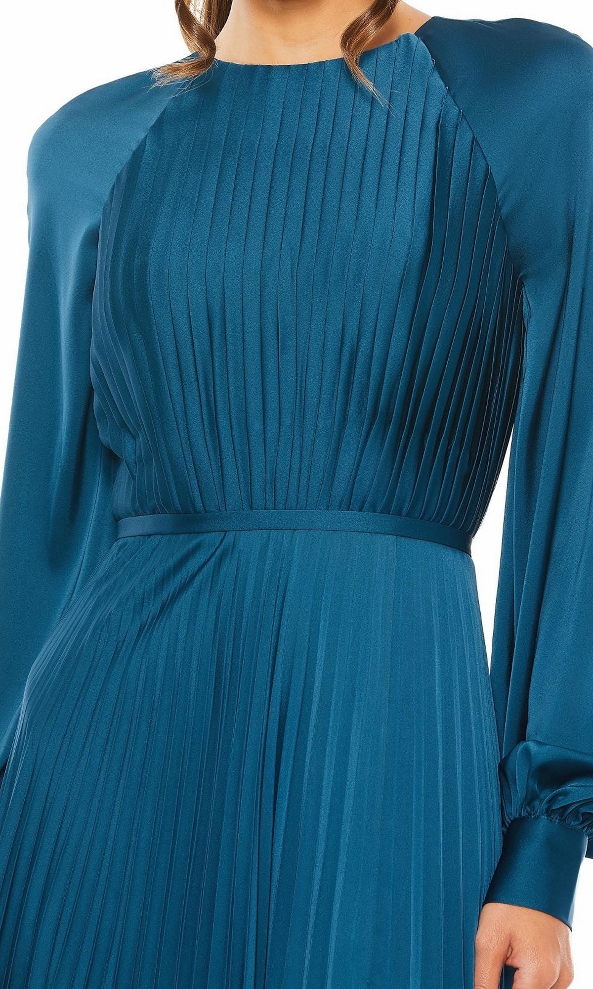 A person wears the Mac Duggal 26590—a modest, long-sleeved teal blue formal dress with pleats, a fitted waist, and a round neckline; only the upper body is visible.