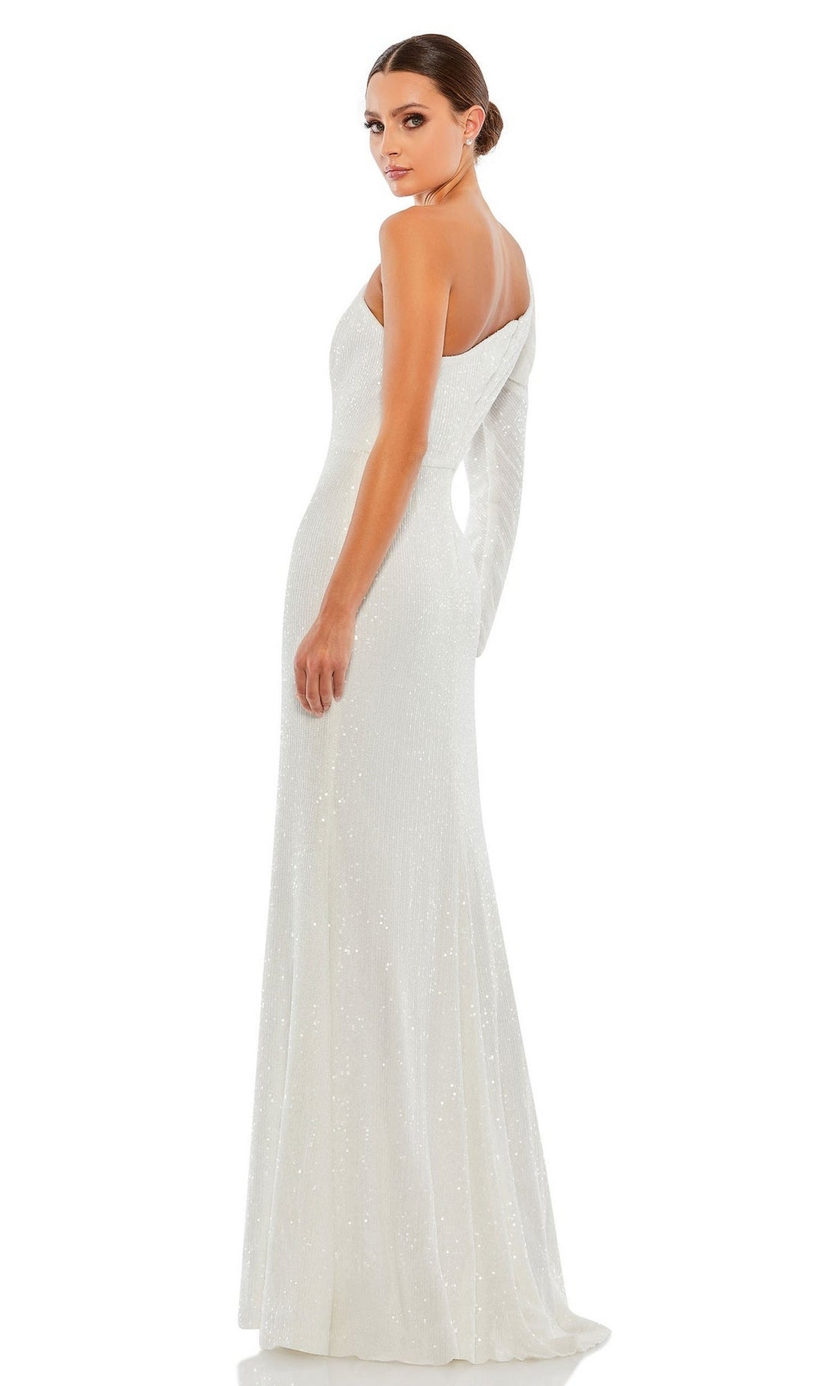 A woman stands gracefully, looking over her shoulder in the Mac Duggal 26591 One-Sleeve Sequin Formal Dress—a white, floor-length gown with subtle shimmer.