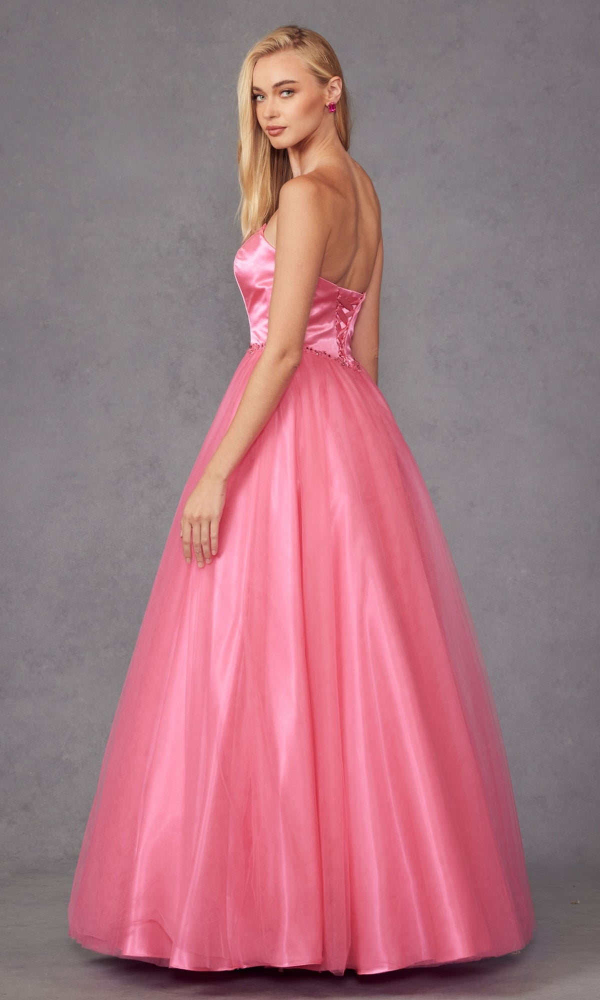 A woman wears the Strapless Sweetheart Long Prom Ball Gown 265 with a corset back, standing against a gray background and looking over her shoulder.