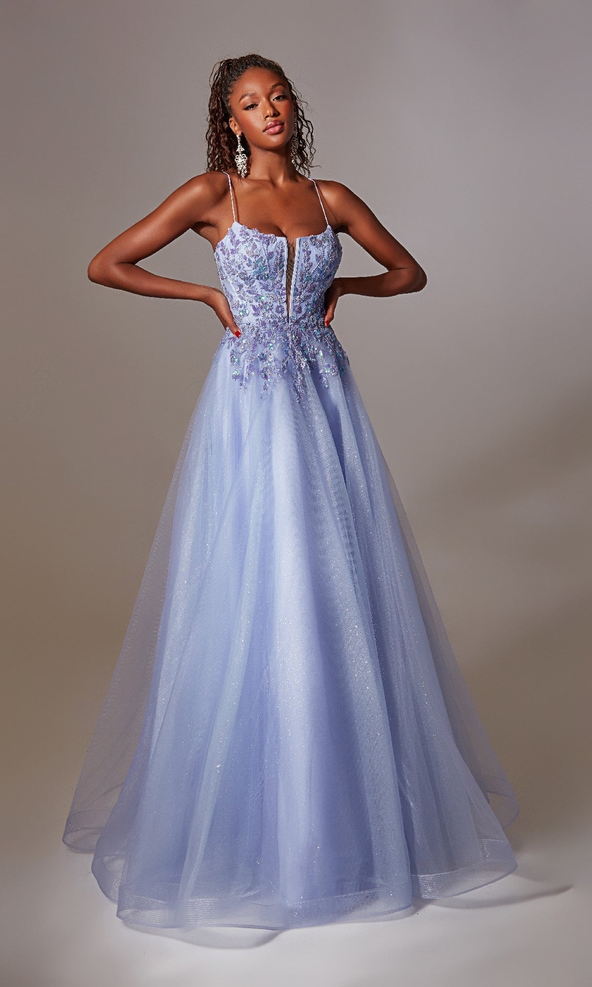 A woman stands hands on hips against a plain background wearing the Deep V-Neck Long Prom Ball Gown: Aerie Couture 265, featuring a light blue floor-length tulle skirt, thin straps, and a fitted beaded bodice.