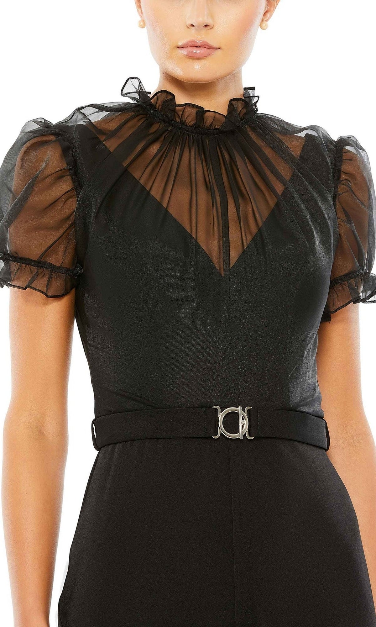 A woman wears the Long Formal Jumpsuit 26621 by Mac Duggal, featuring a black design with sheer puff sleeves, a ruffled high neckline, and a belted waist with a metallic buckle.
