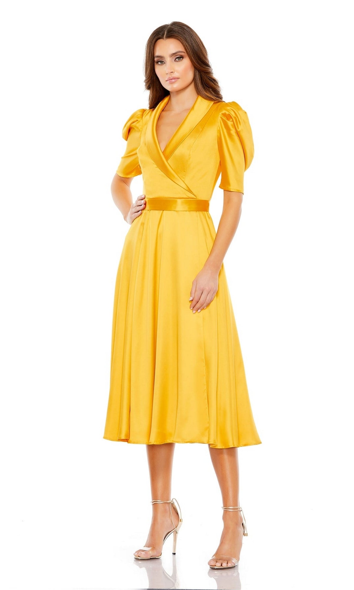 A woman wearing the Mac Duggal 2628 Short Sleeve Wedding Guest Dress—a yellow, satin, tea-length dress with short puff sleeves and a wrapped V-neckline—paired with silver high-heeled sandals.