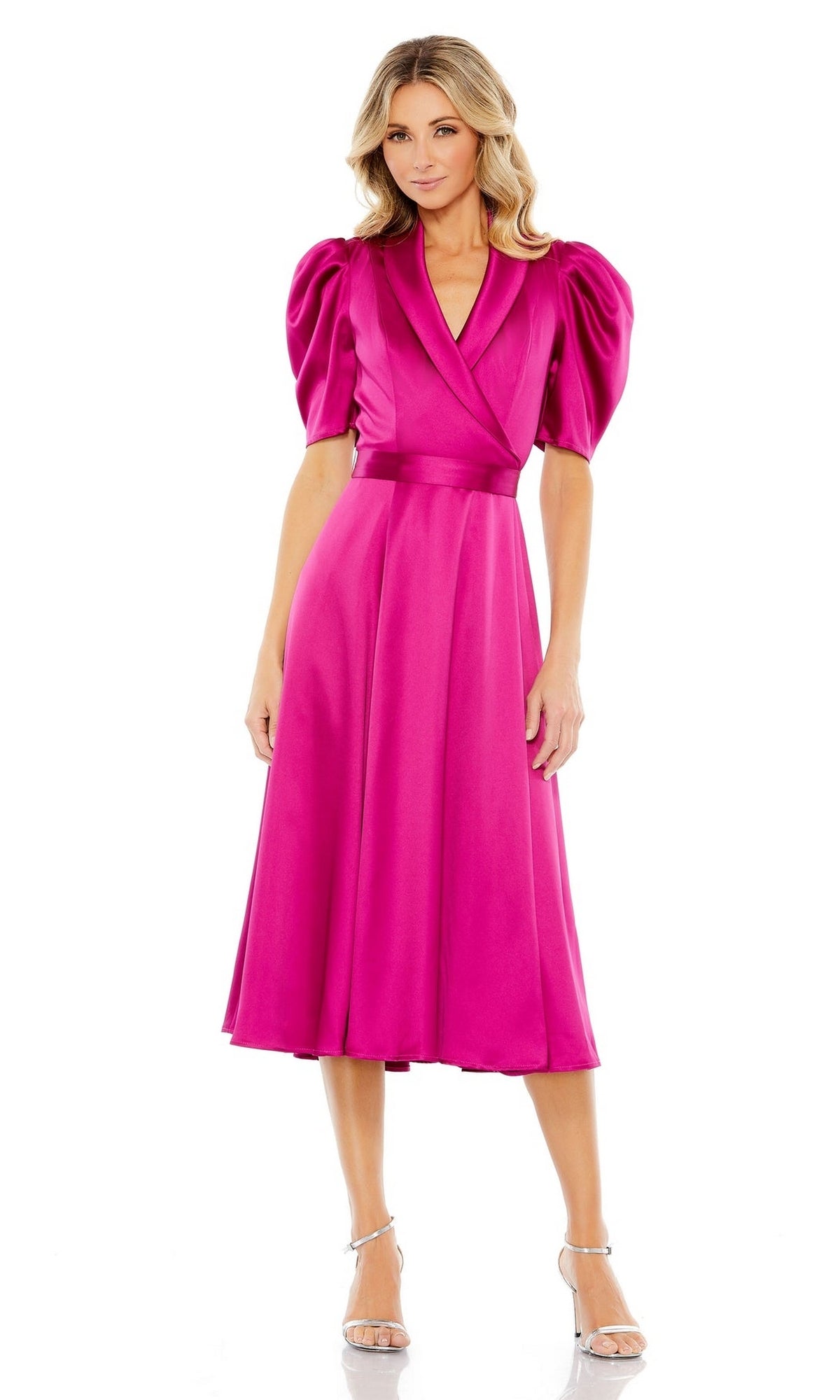 A woman wears the Mac Duggal 2628, a bright pink tea-length satin dress with puffed short sleeves and a V-neckline, paired with silver heels—an elegant wedding guest look.