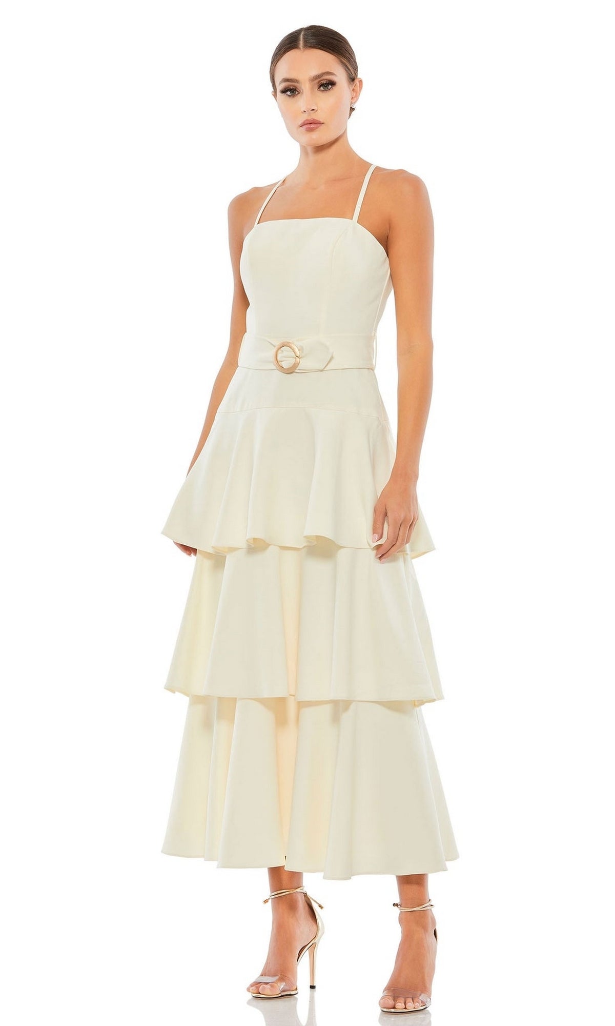 A woman models the Short Wedding Guest Dress 26629 by Mac Duggal, a cream-hued, ruffle-layered dress with a belted waist and spaghetti straps, paired with metallic high-heeled sandals against a white background.