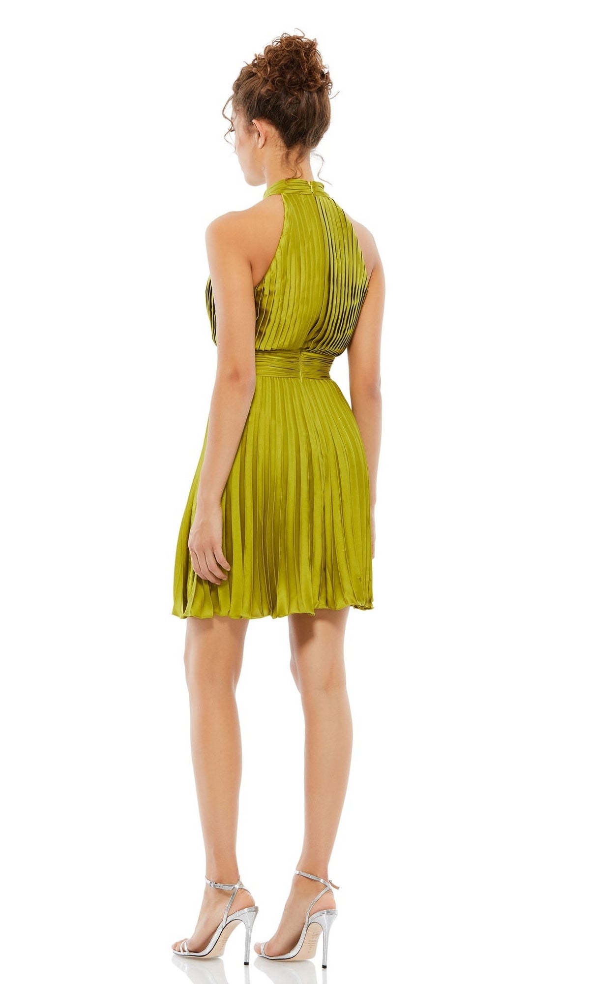 A woman stands with her back to the camera against a white background, wearing the Mac Duggal 26645 Short Pleated Hoco Dress— a sleeveless, knee-length green dress—paired with silver high-heeled sandals.