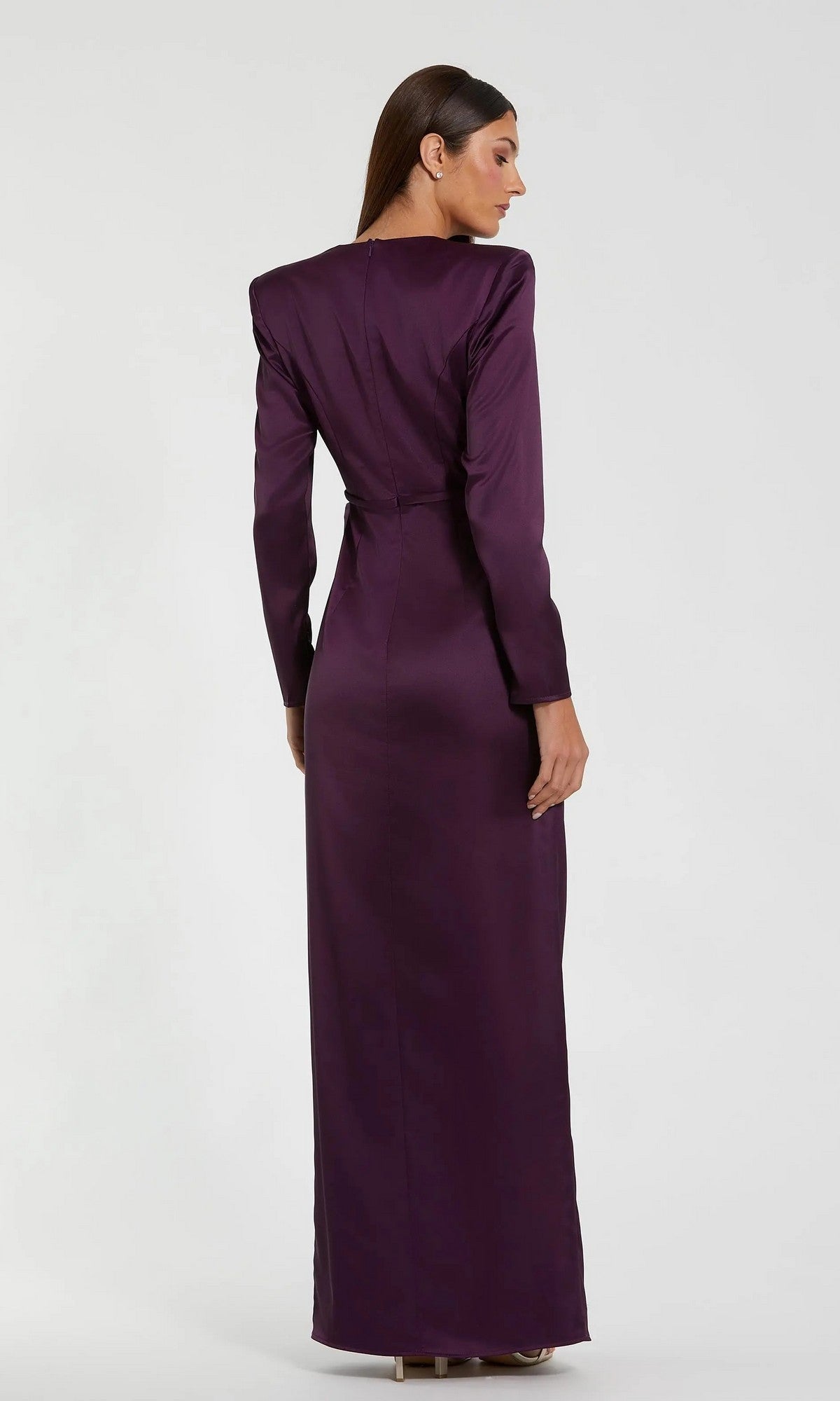 A woman, seen from behind, wears the Mac Duggal 26676 Bold-Shoulder Long Formal Dress in purple. With padded shoulders and a tailored fit, it shapes an elegant silhouette against a plain light backdrop.