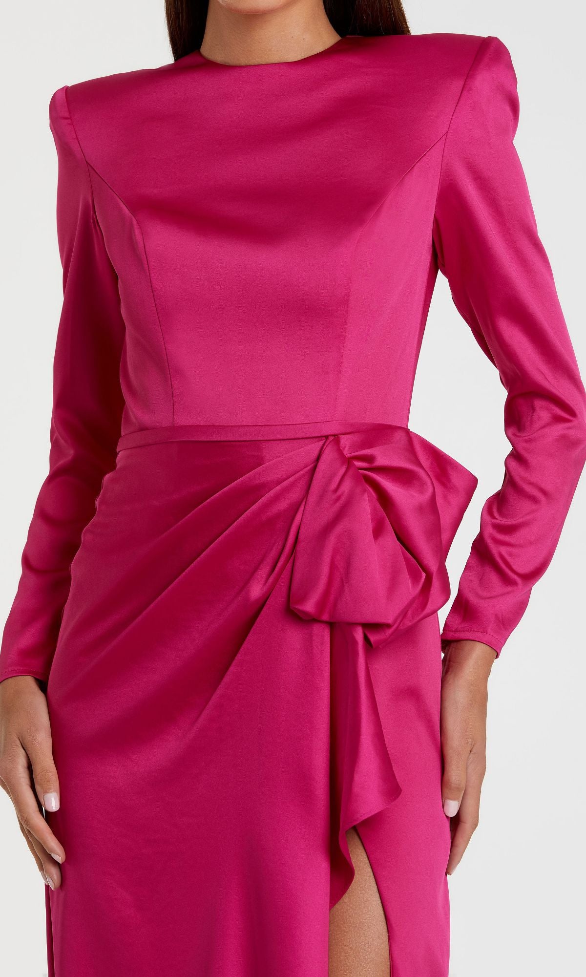 A woman wears the Mac Duggal 26676 Bold-Shoulder Long Formal Dress—a bright pink satin gown with long sleeves, structured shoulders, a large waist bow, and thigh-high slit. This bra-friendly dress is perfect for formal occasions.
