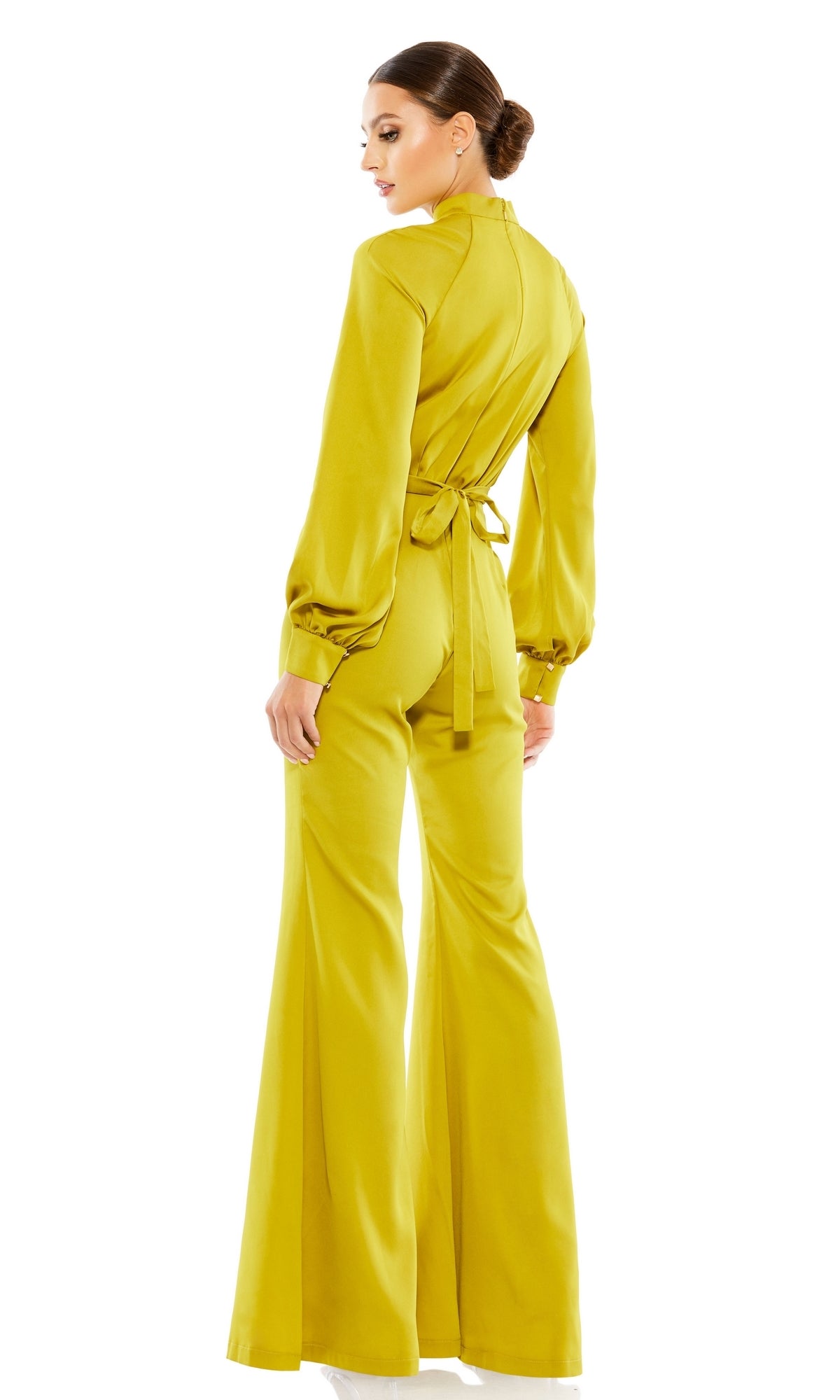 A woman stands facing away, wearing the Mac Duggal Long Formal Jumpsuit 26685 in chartreuse, featuring long sleeves, a tie-back waist, flared legs, and her hair styled in a low bun.