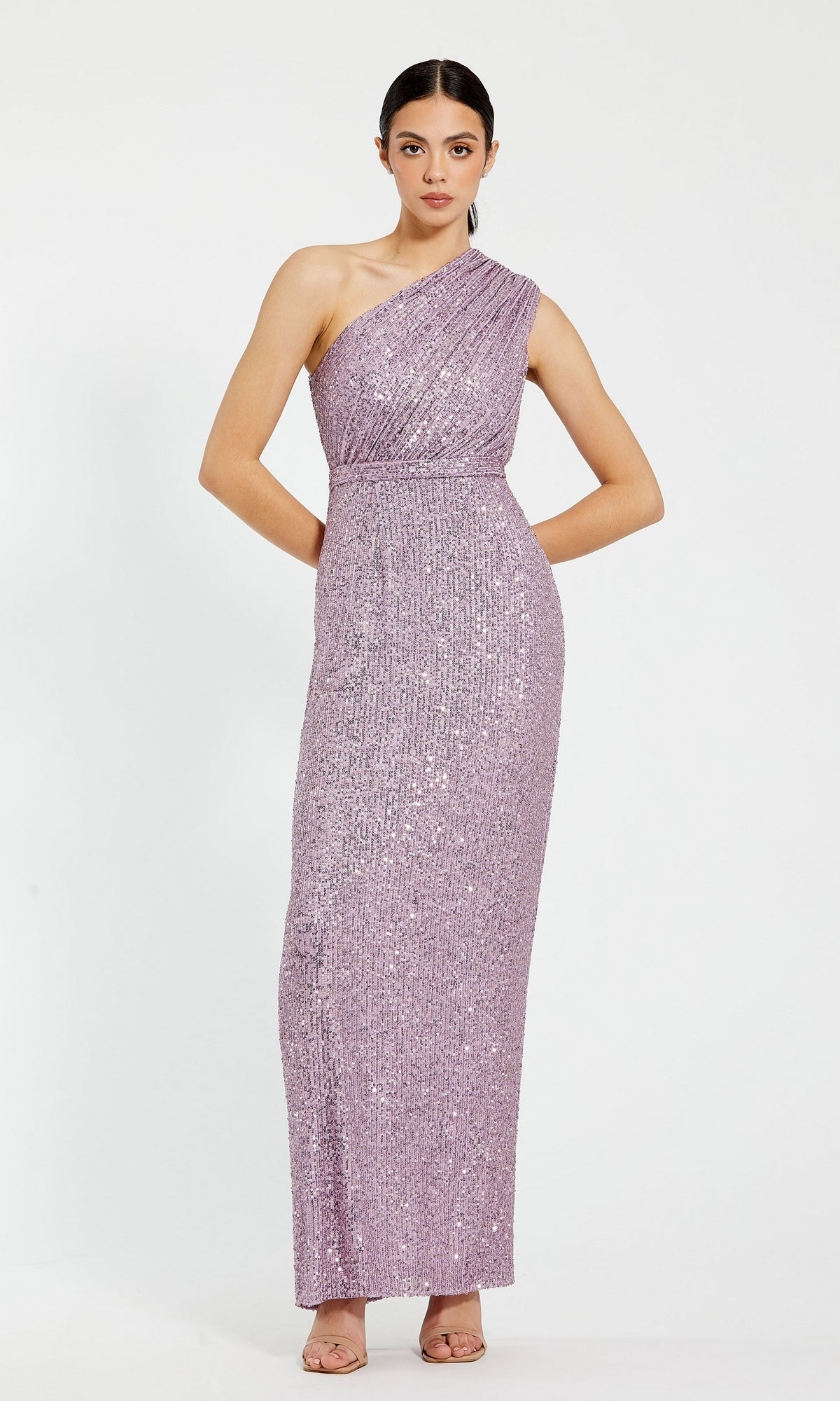 A woman poses against a plain white background wearing the Mac Duggal 26694: a floor-length, one-shoulder, fitted sequin formal dress in light purple, paired with open-toe heels.