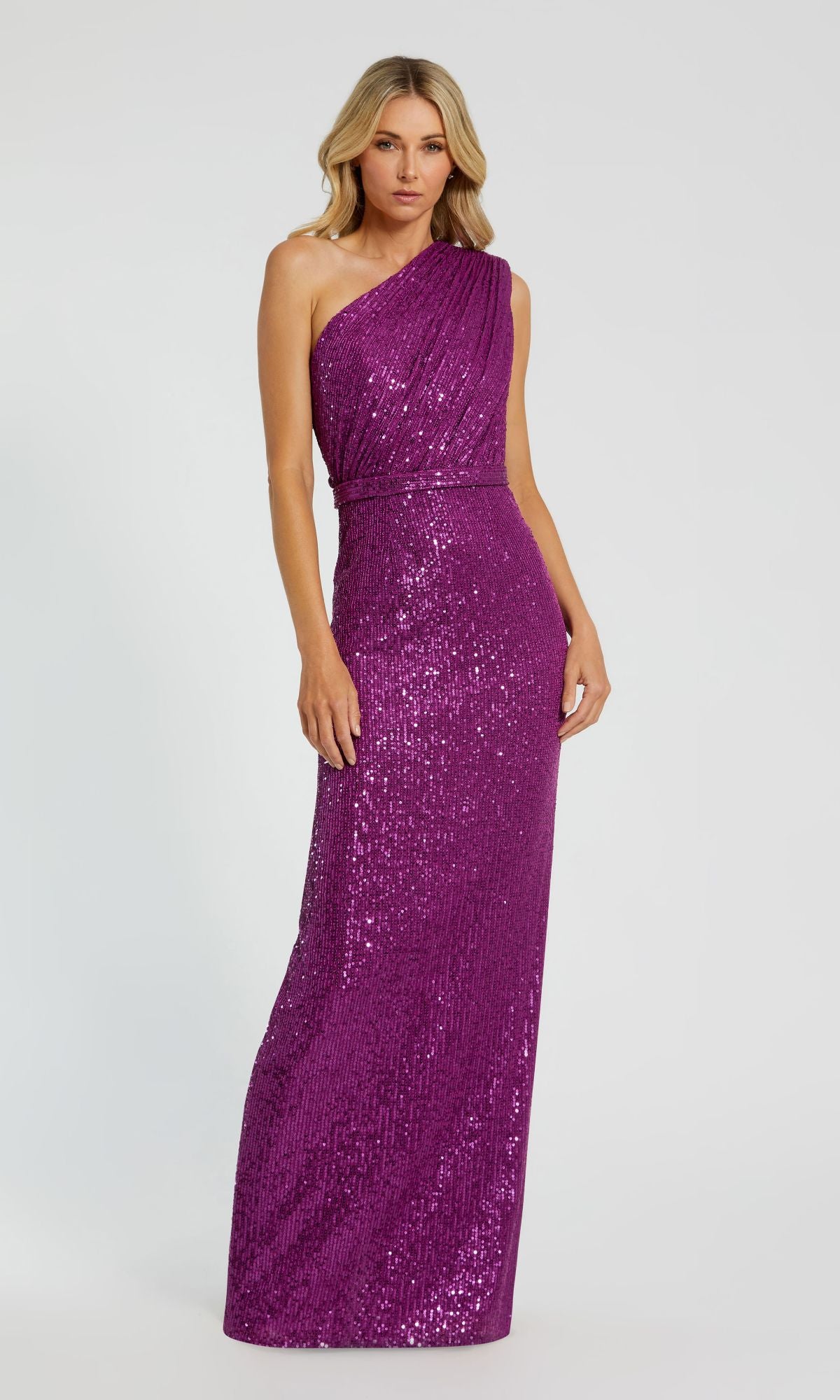 A woman wearing the Mac Duggal 26694 one-shoulder, floor-length purple sequin formal dress stands against a plain light background.