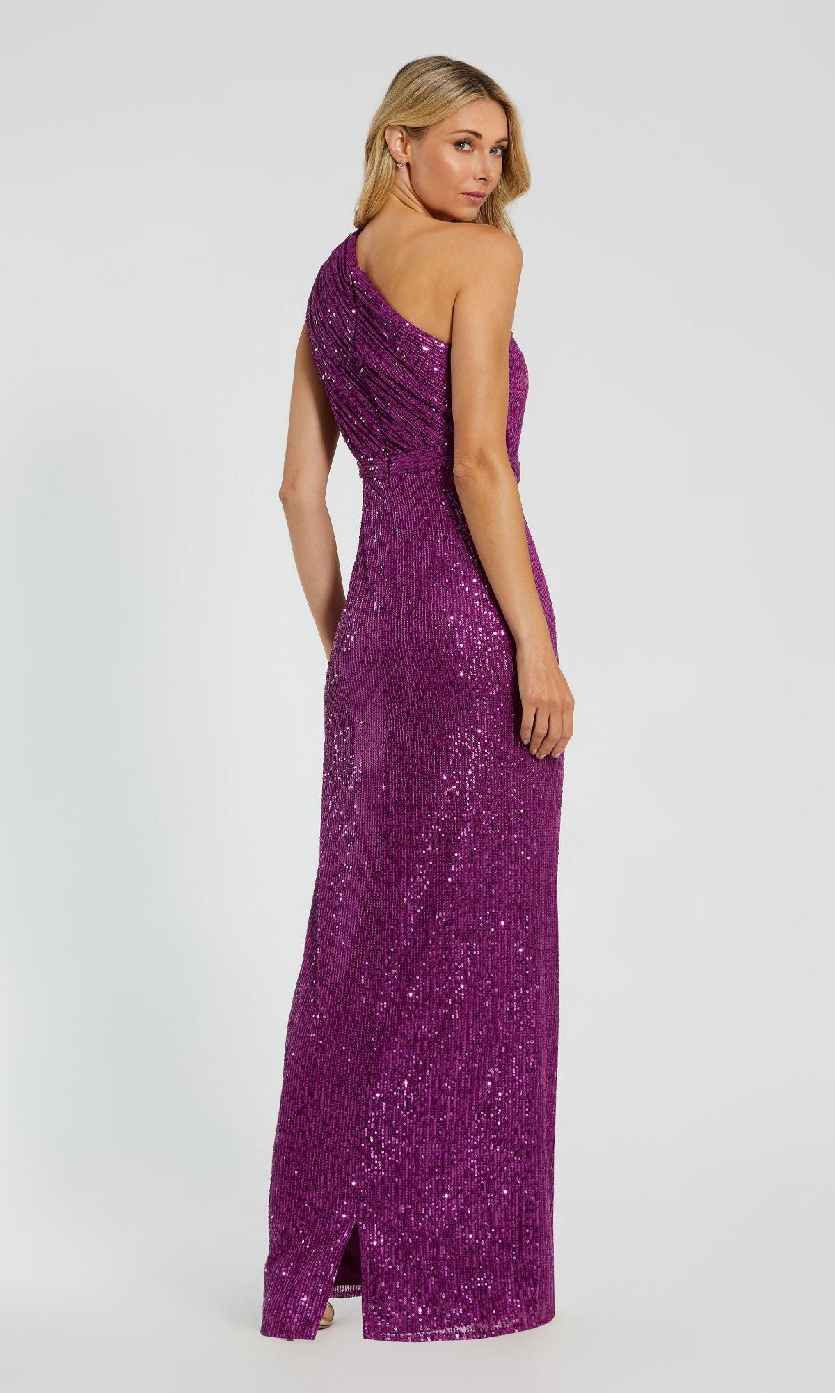 A woman models the Mac Duggal 26694, a purple, floor-length one-shoulder sequin formal dress with a back slit, posed against a plain light background.