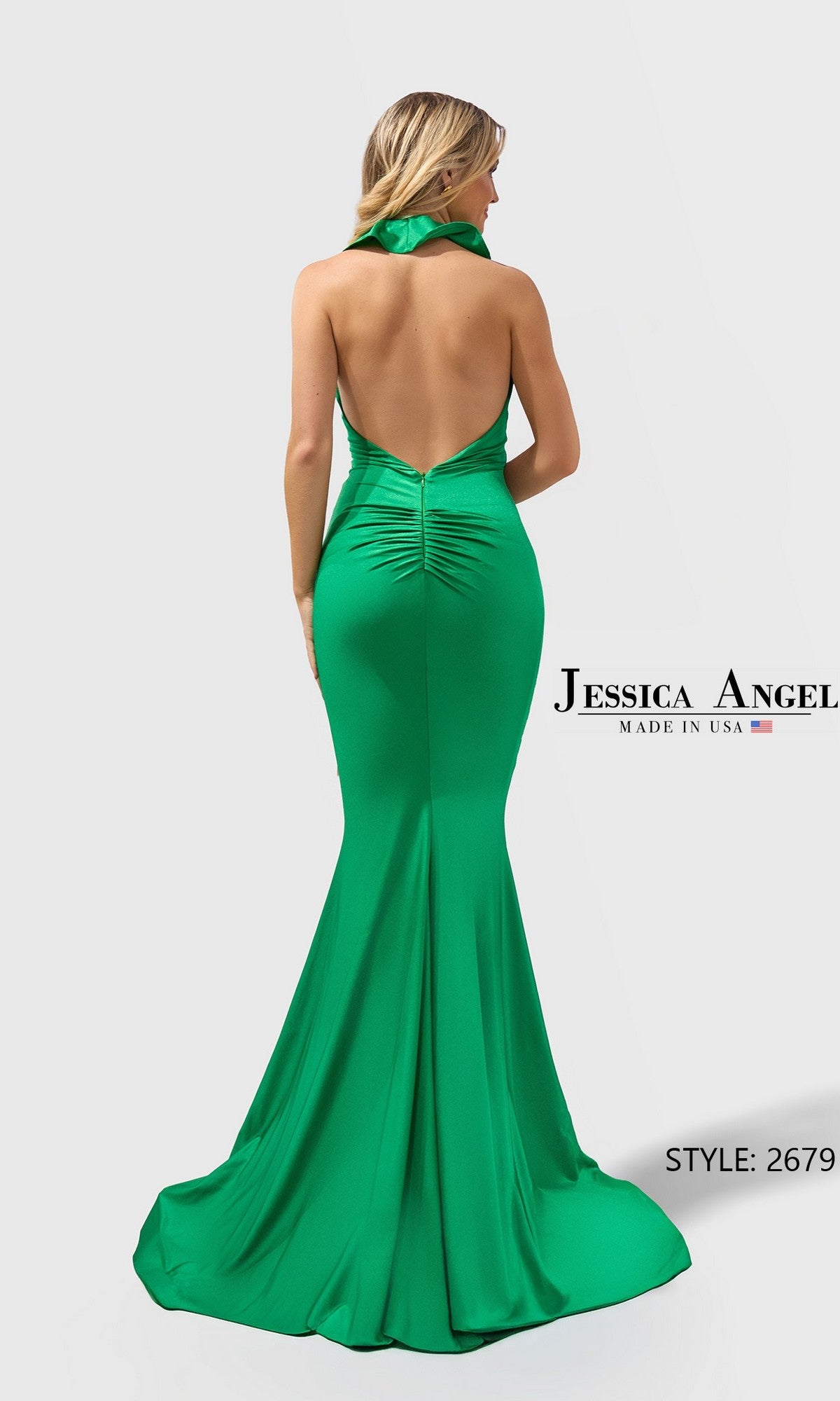 A woman stands with her back to the camera, wearing a green, backless halter mermaid gown labeled