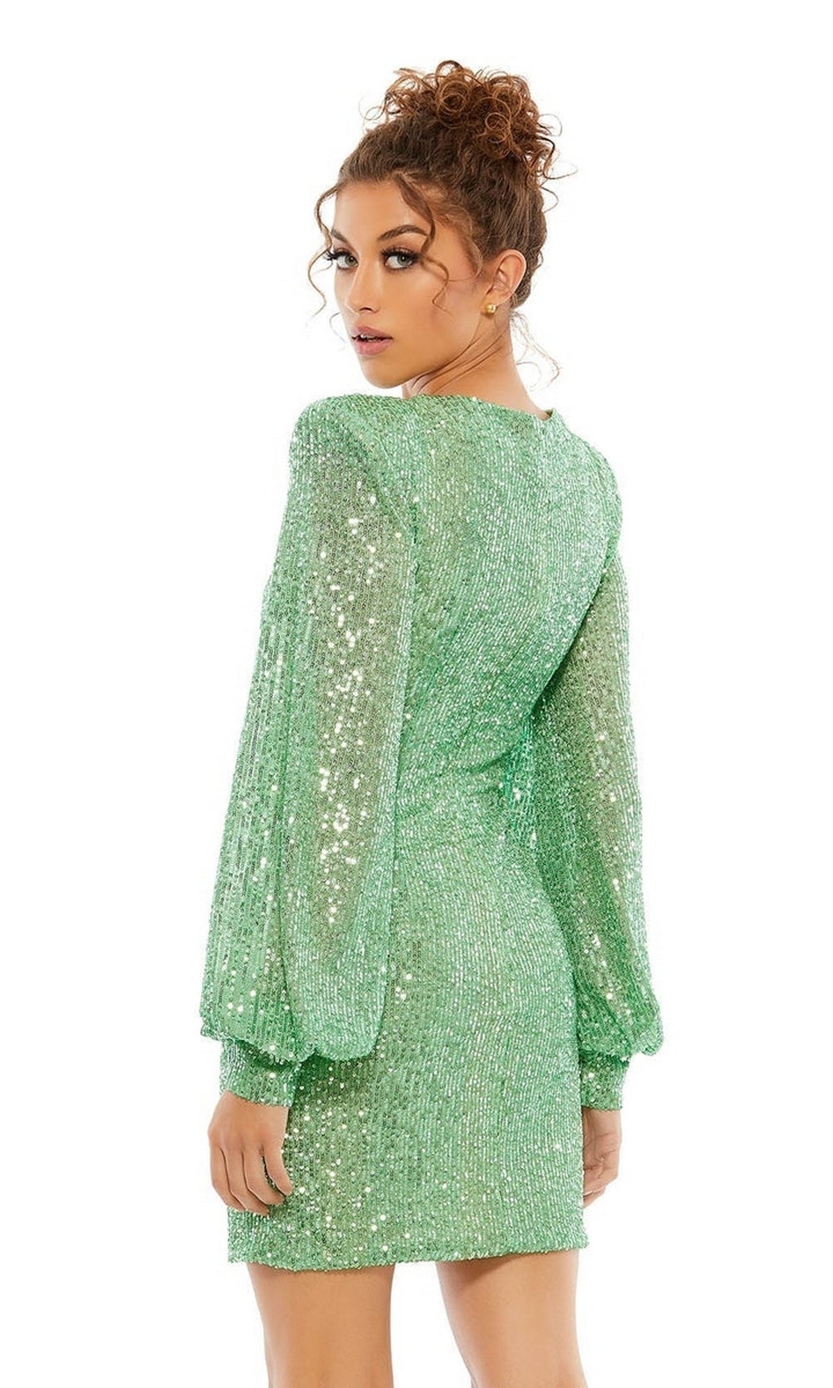 A woman with curly hair in an updo wears the Long Sleeve Sequin Hoco Dress: Mac Duggal 26865, a short fitted green dress that sparkles as she turns slightly to the side and looks over her shoulder.